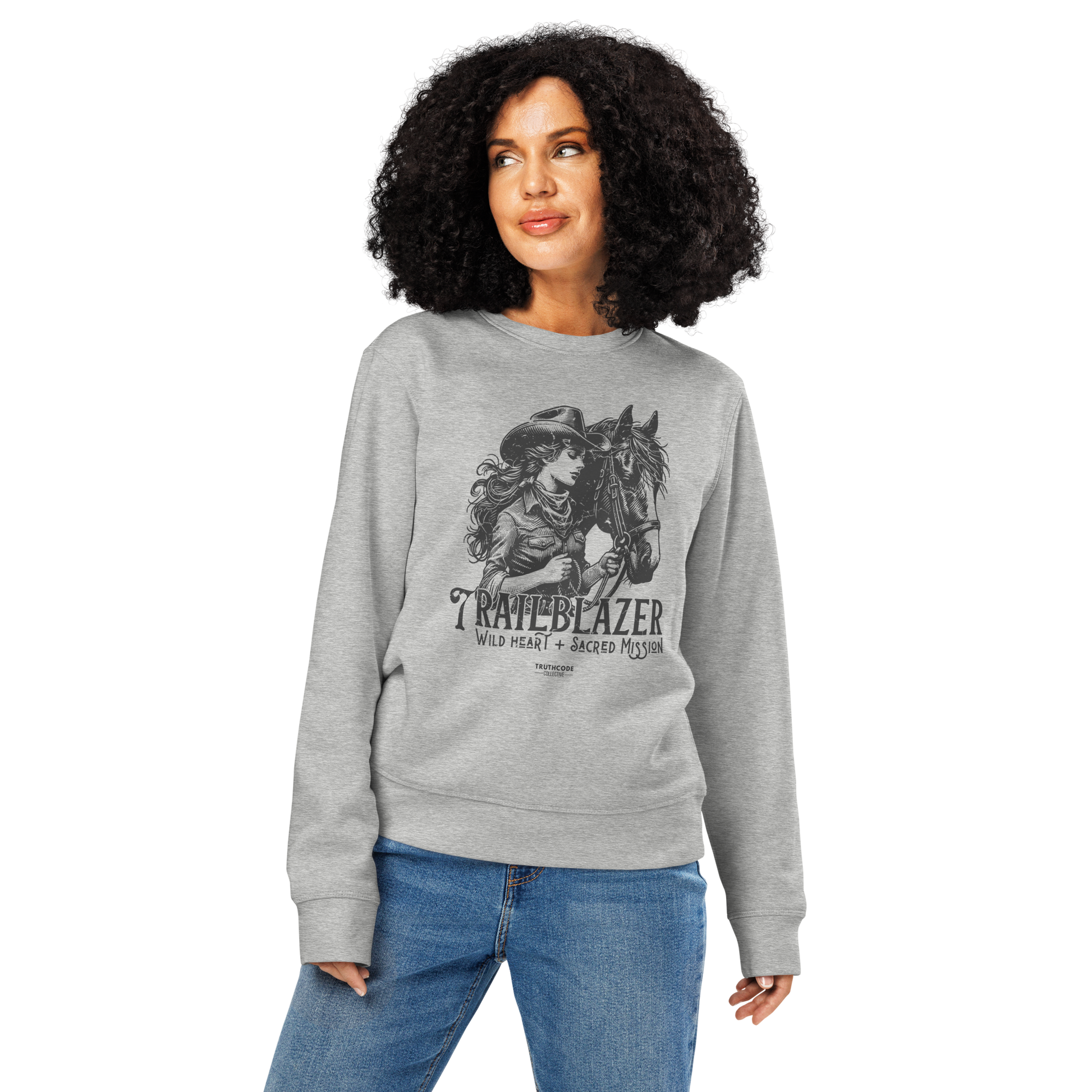Woman wearing gray organic sweatshirt with graphic of a woman holding a horse and text 'Trailblazer' and 'Wild heart, sacred mission' on a white background