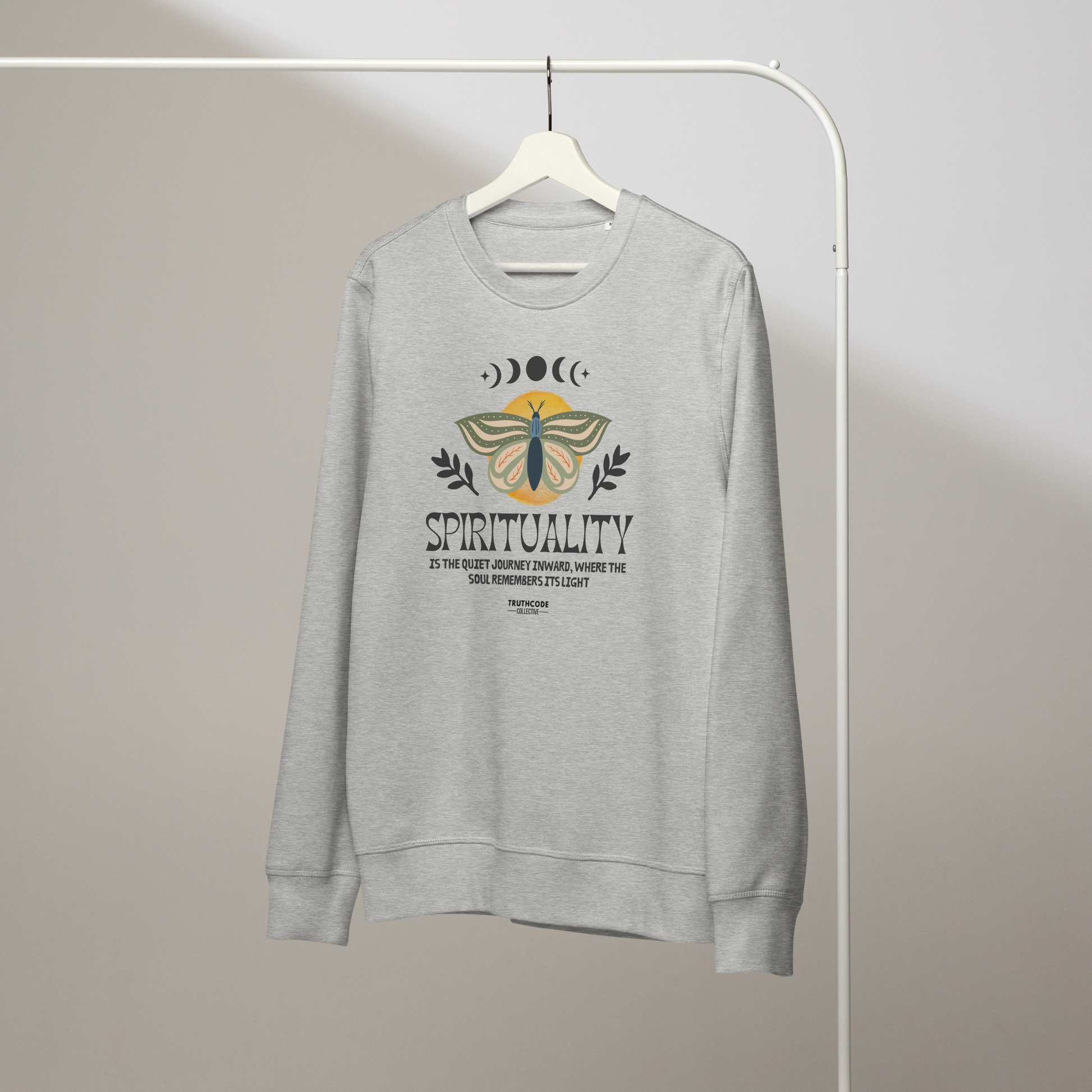 Gray organic sweatshirt with a butterfly design and text 'Spirituality is the quiet journey inward, where the soul remembers it's light' on a white hanger with a gray wall background 
