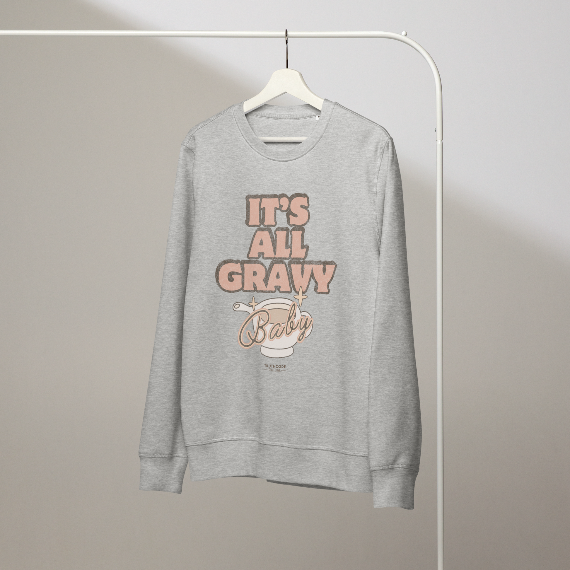 Gray organic sweatshirt with 'It's All Gravy Baby' text and graphic design of a gravy boat on a white hanger with a gray wall background