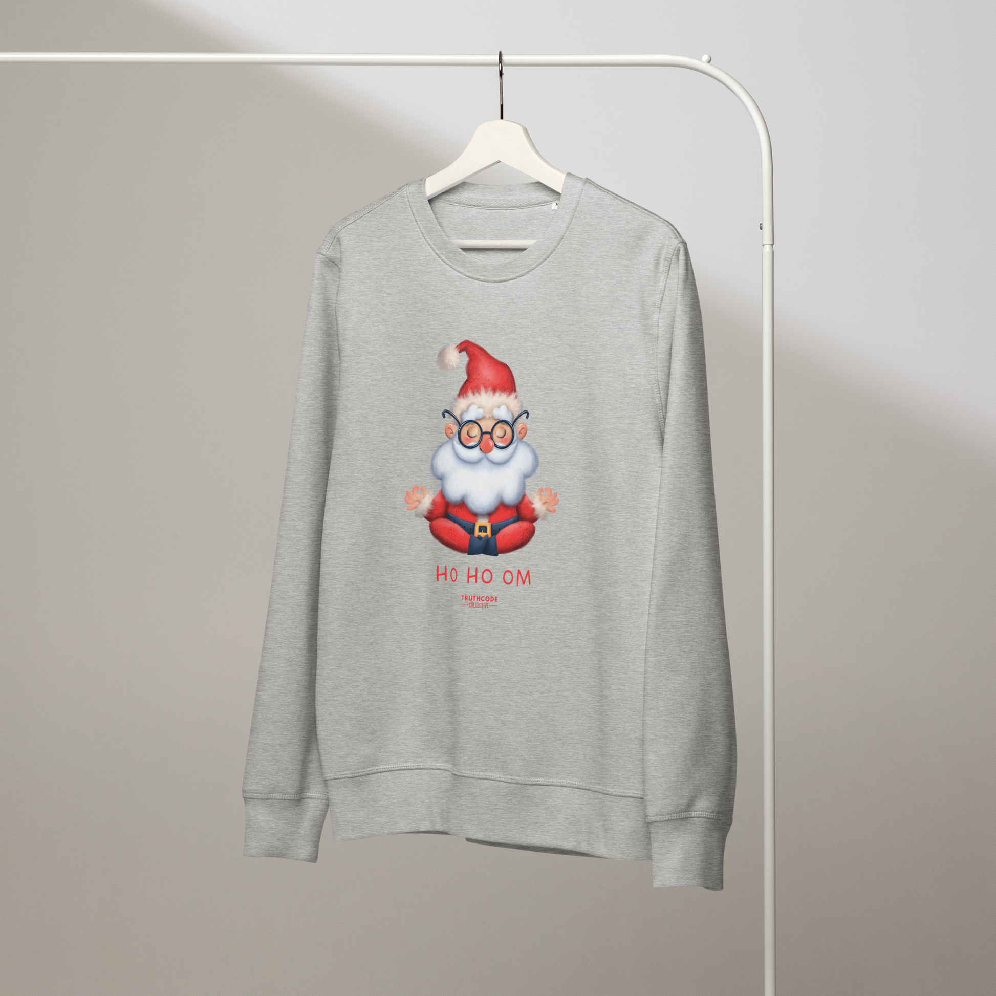 Gray organic sweatshirt with a cartoon Santa Claus meditating design and text 'HO HO OM' on a hanger with a gray wall background