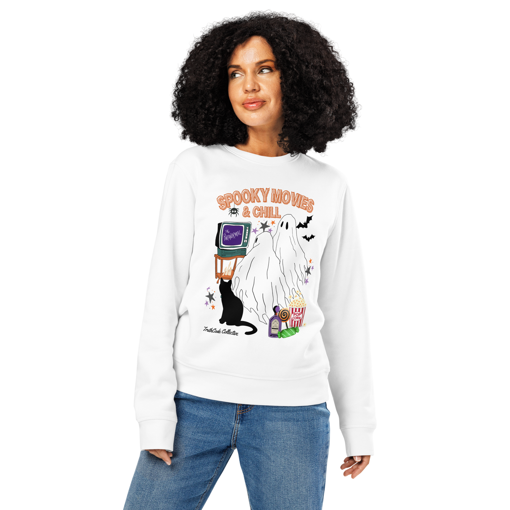 Woman wearing white organic sweatshirt with Halloween-themed design featuring a ghost, black cat, TV, and popcorn and text 'Spooky movies and chill' on a white background
