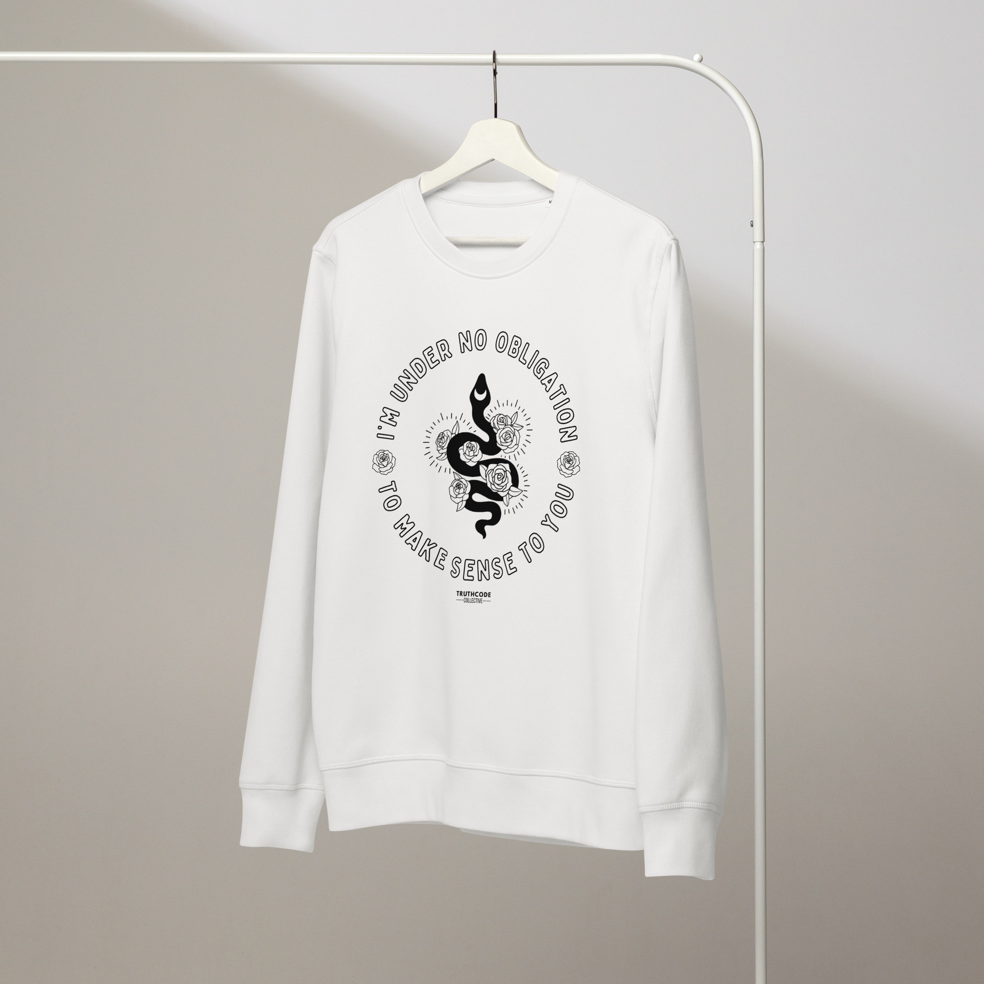White organic sweatshirt with black graphic snake and floral design and text reading 'I'm under no obligation to make sense to you' on a hanger with gray wall background