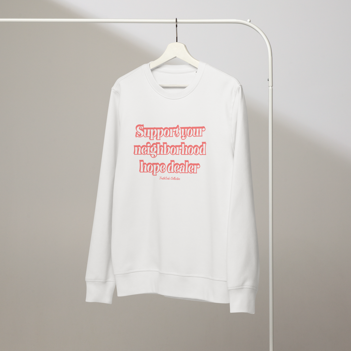 White organic sweatshirt with text 'Support your neighborhood hope dealer' on a white hanger with a gray wall background