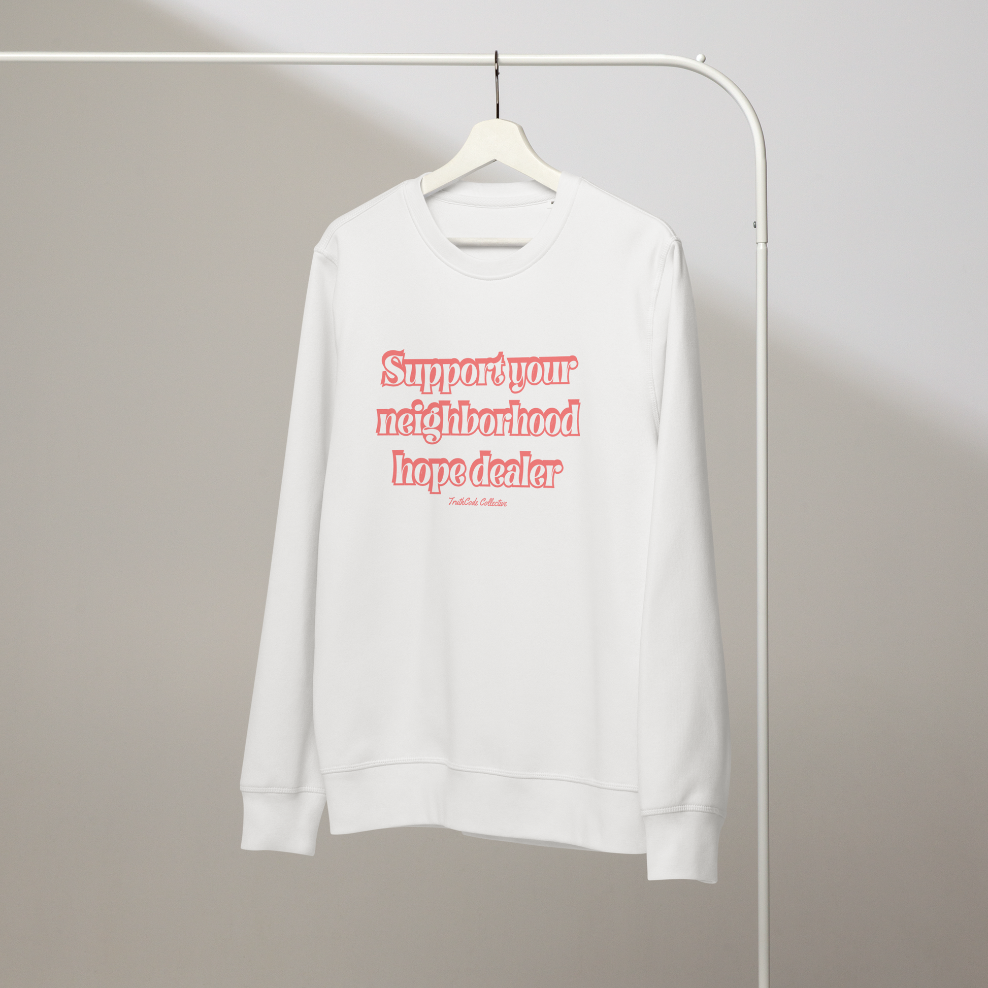 White organic sweatshirt with text 'Support your neighborhood hope dealer' on a white hanger with a gray wall background