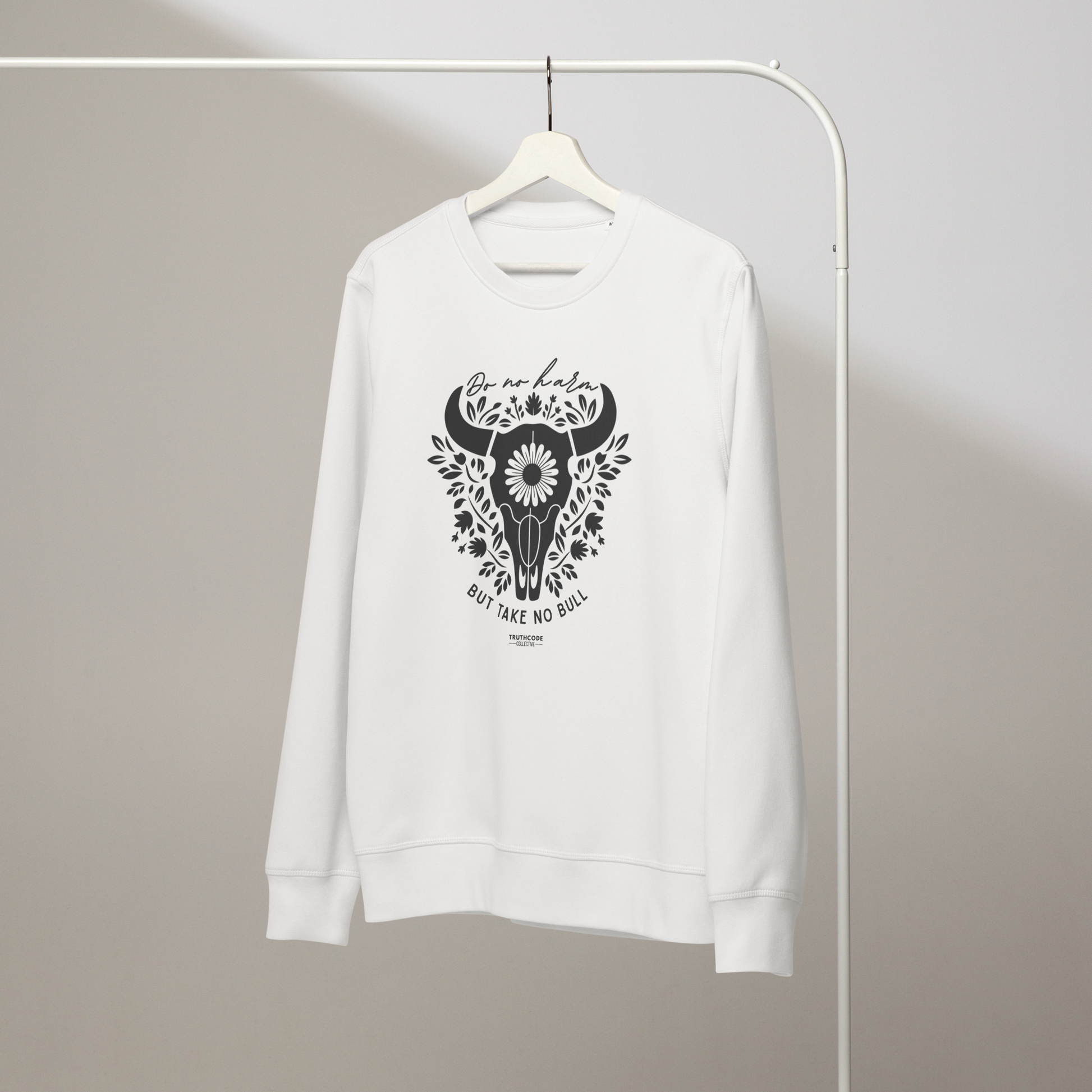 White organic sweatshirt with bull skull and floral design and text 'Do no harm, but take no bull' on a white hanger with a gray wall background