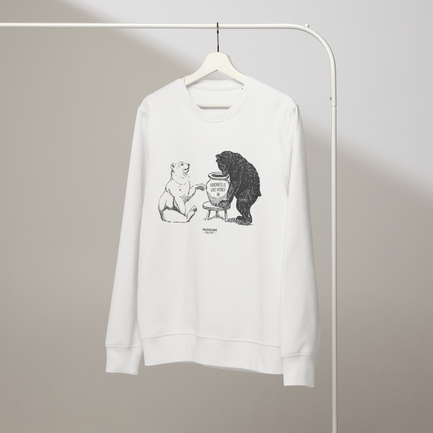 White organic sweatshirt with bears eating honey graphic and text 'Kindness is like honey' on a white hanger with a gray wall background