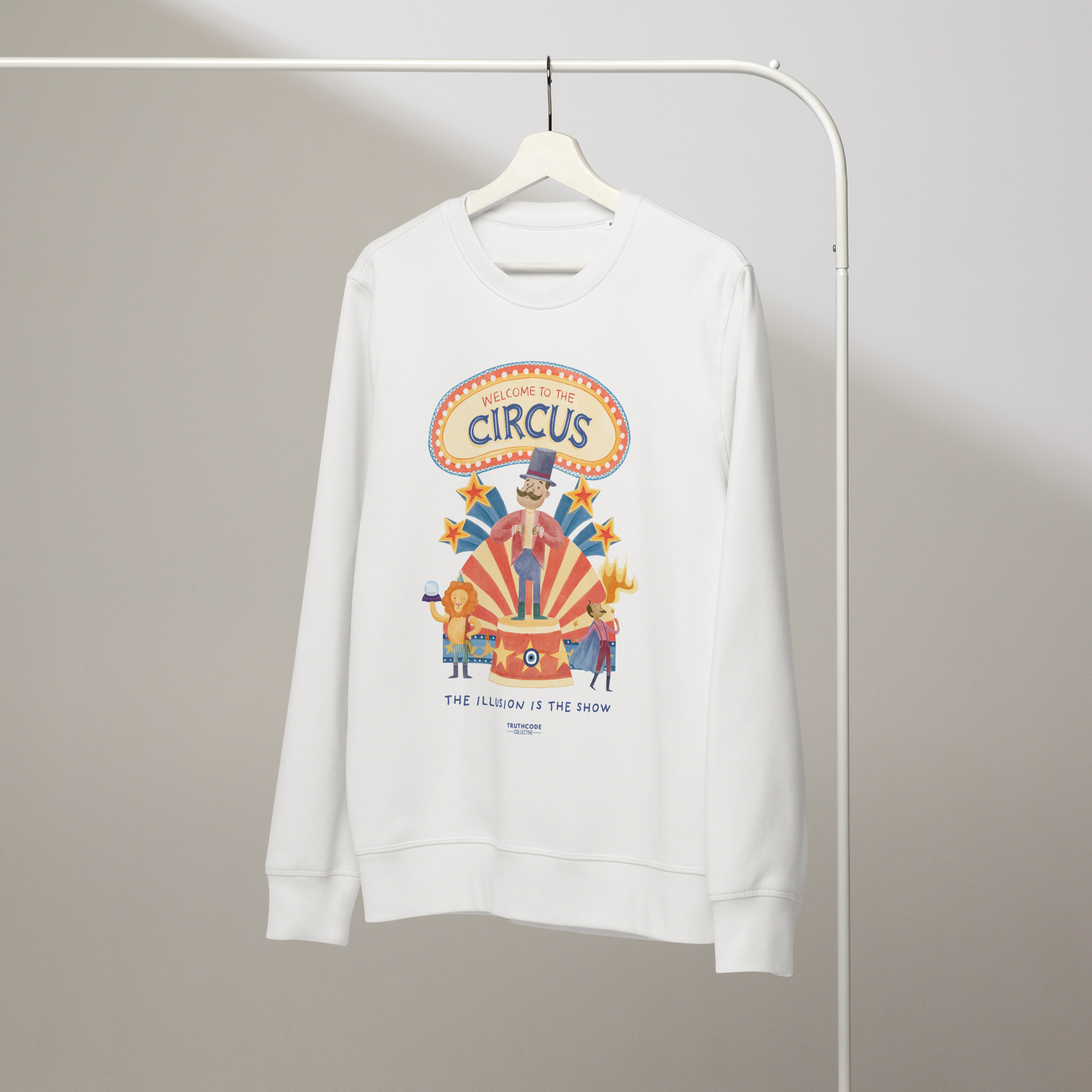 White organic sweatshirt with circus-themed graphic design and text 'Welcome to the circus' and 'The illusion is the show' on a white hanger with a gray wall background
