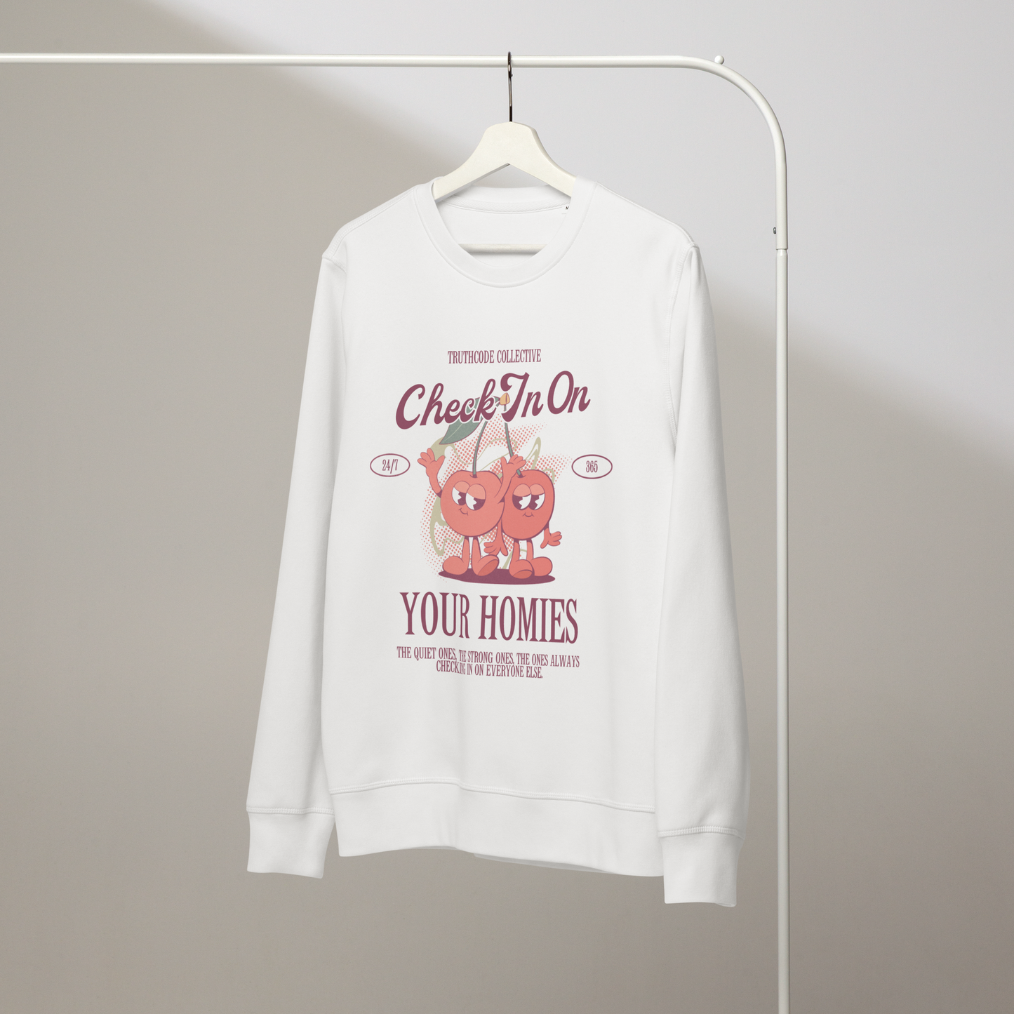 White organic sweatshirt with cartoon cherries and text 'Check in on your homies' on a white hanger with a gray wall background