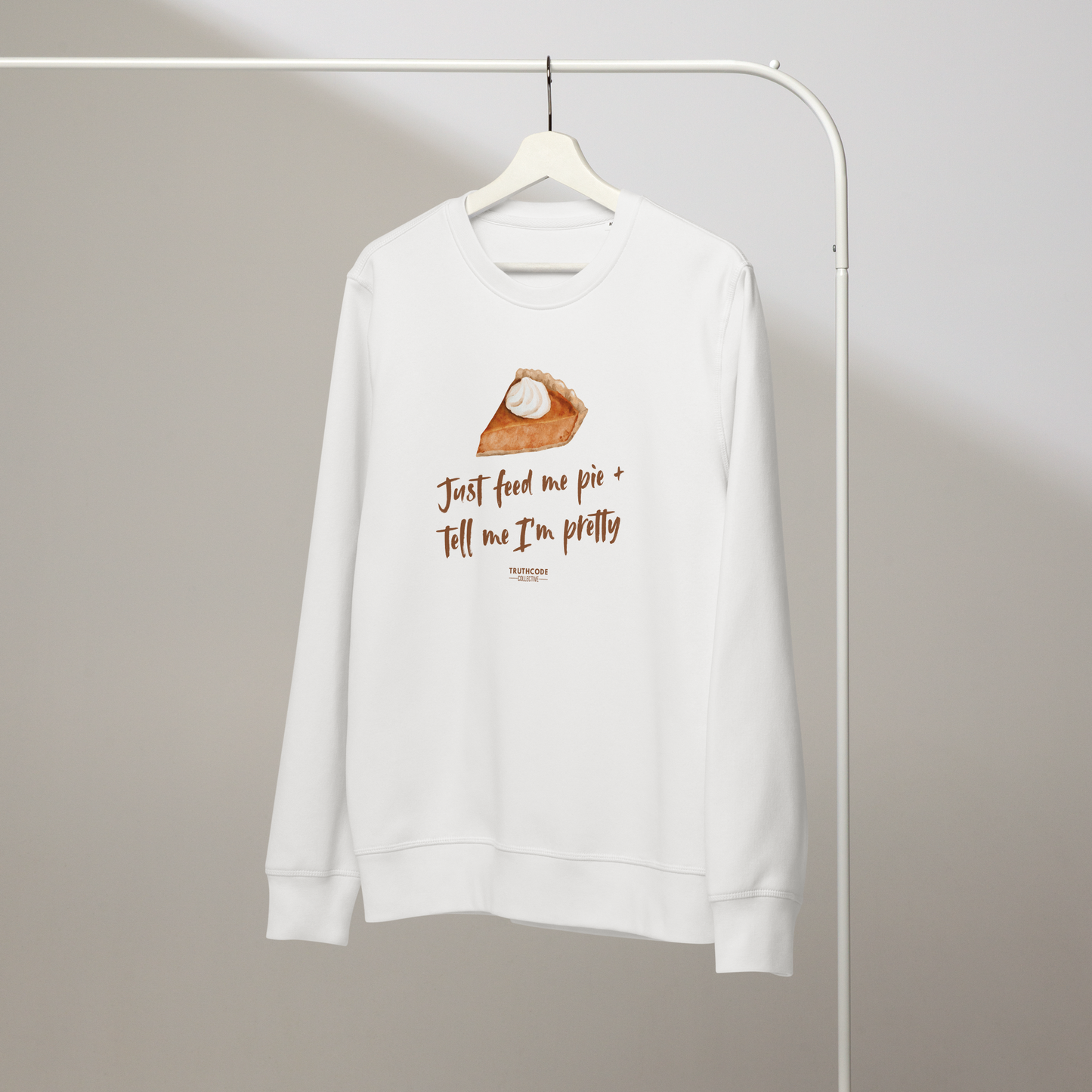 White organic sweatshirt with a pie graphic and text 'Just feed me pie and tell me I'm pretty' on a white hanger with a gray wall background