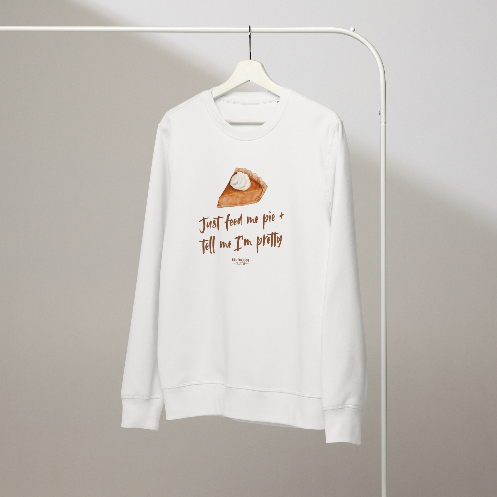 White organic sweatshirt with a pie graphic and text 'Just feed me pie and tell me I'm pretty' on a white hanger with a gray wall background