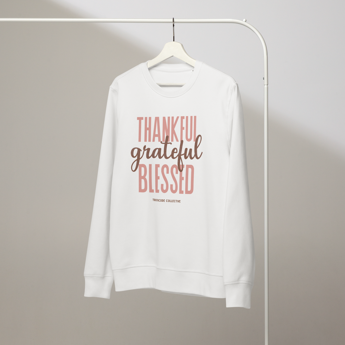 White organic sweatshirt with 'Thankful grateful BLESSED' text on a white hanger with a gray wall background