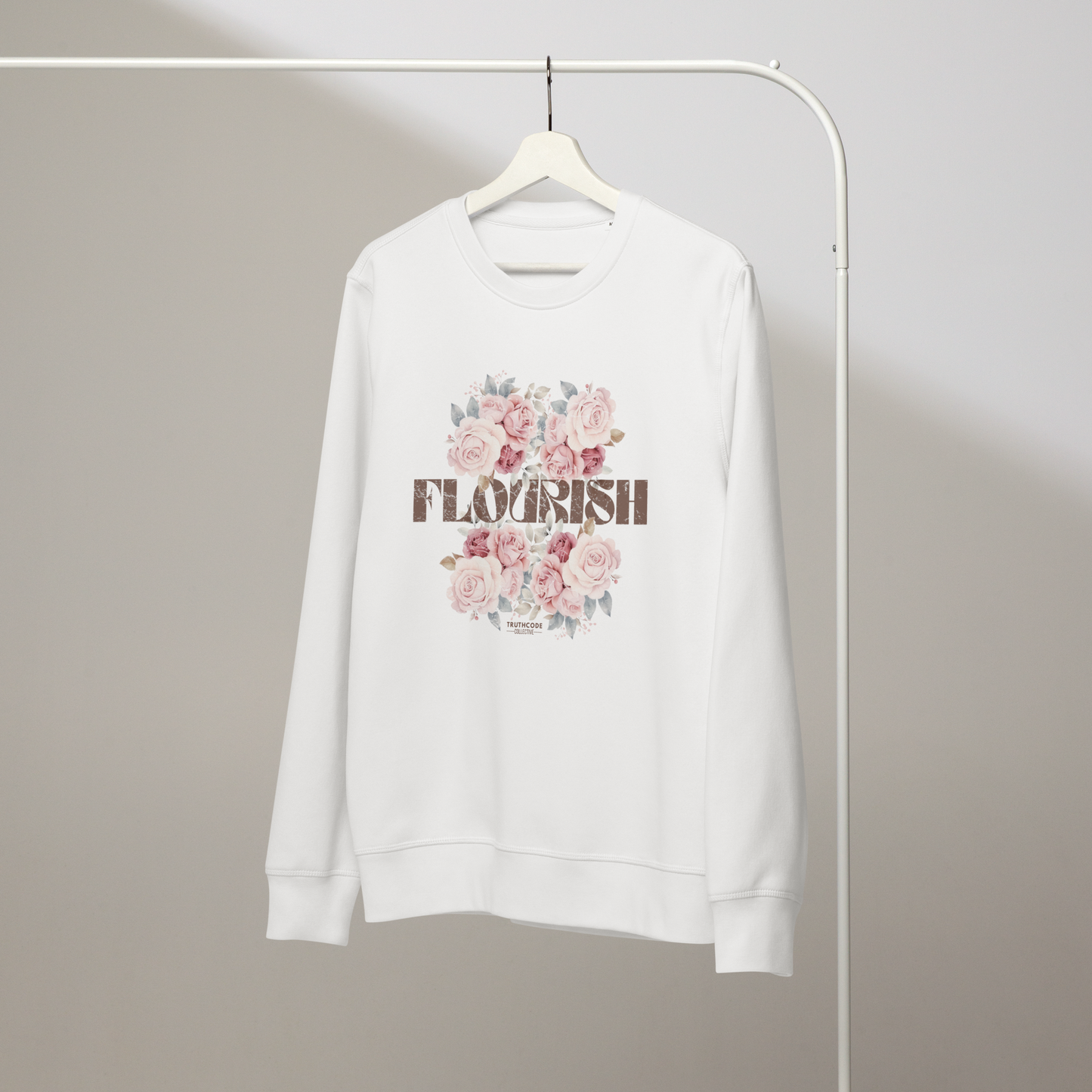 White organic sweatshirt with floral design and 'Flourish' text on a white hanger with a gray wall background