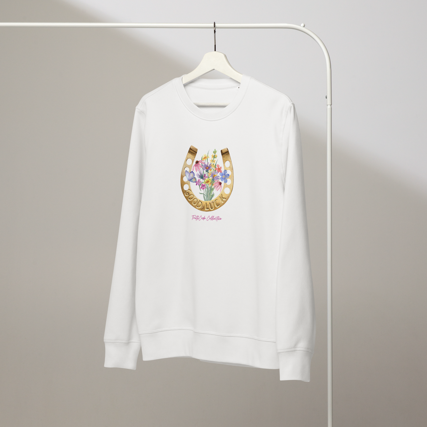 White organic sweatshirt with a floral and horseshoe design and text 'GOOD LUCK' on a white hanger with a gray wall background