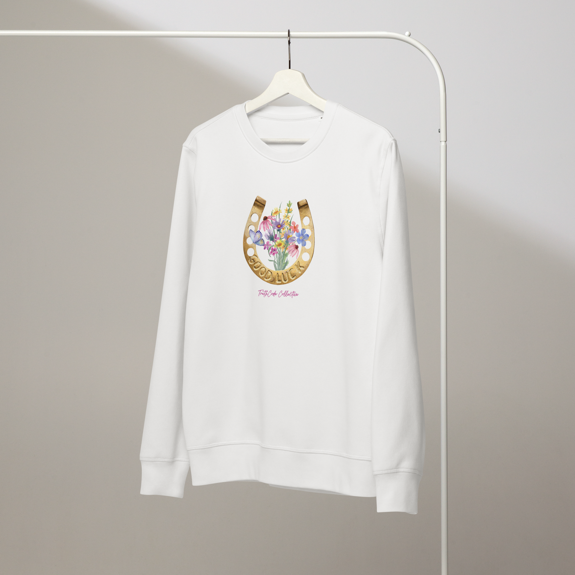 White organic sweatshirt with a floral and horseshoe design and text 'GOOD LUCK' on a white hanger with a gray wall background