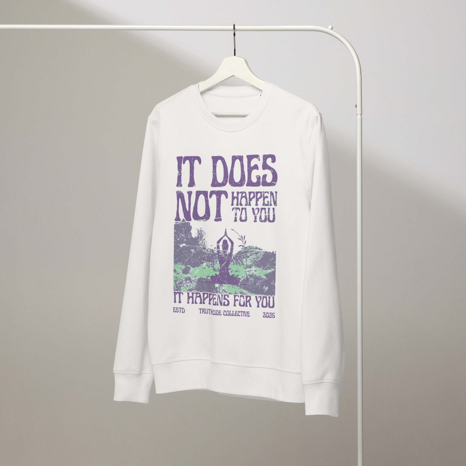White organic sweatshirt with person meditating in nature graphic design and text 'It dos not happen to you, it happens for you' on a white hanger with a plain wall background