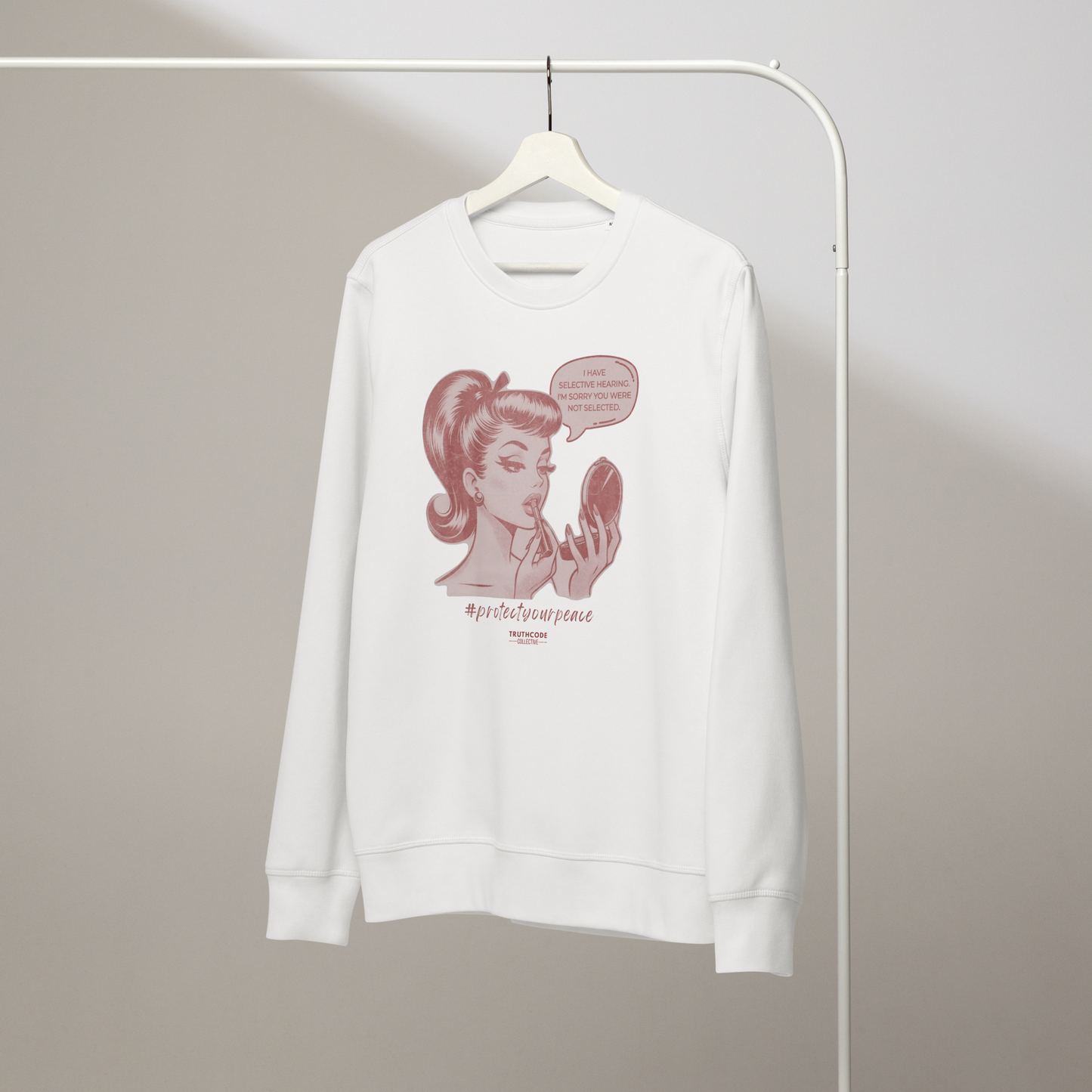 White organic sweatshirt with a vintage style graphic of a woman and text 'I have selective hearing. I'm sorry you weren't selected' on a hanger with a plain wall background