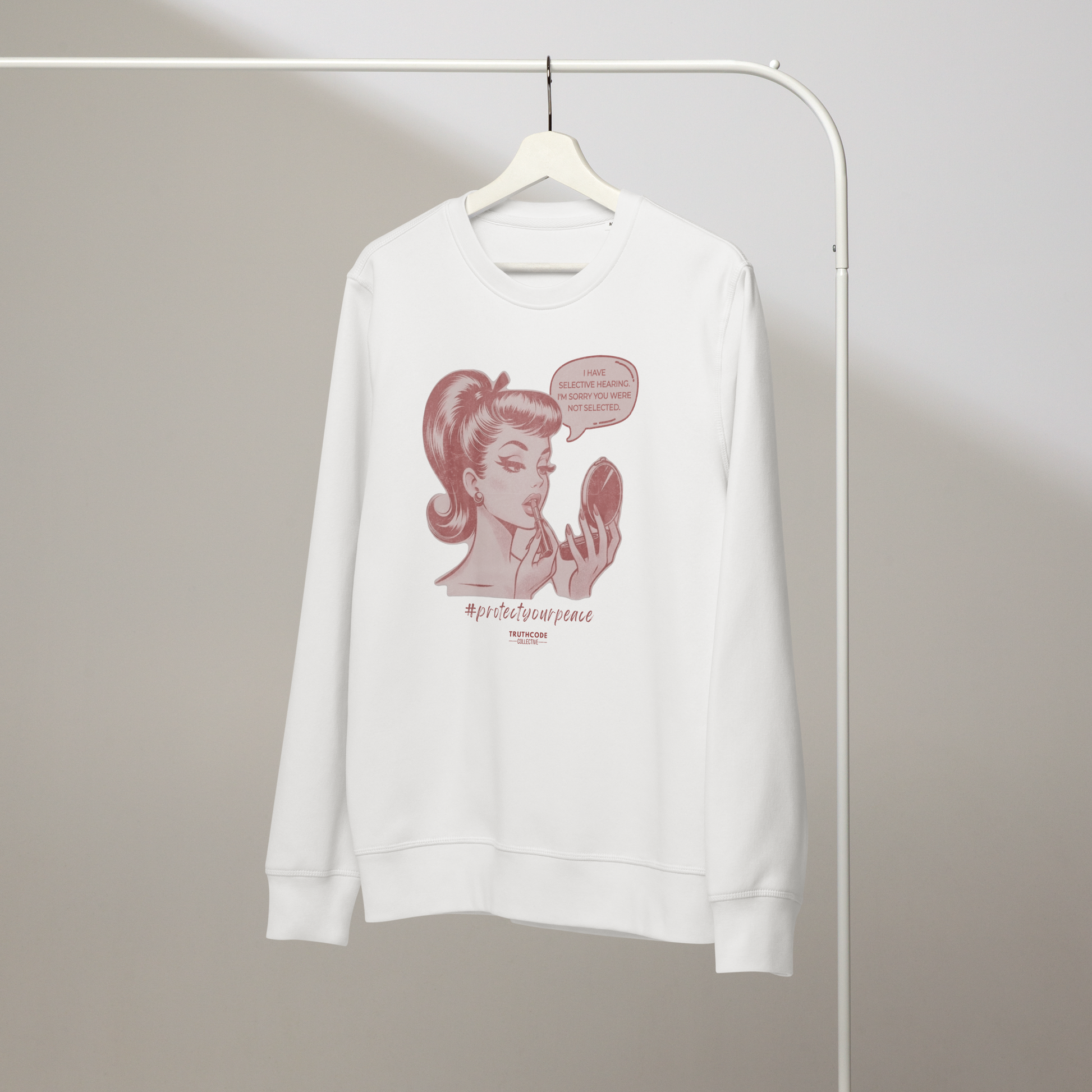 White organic sweatshirt with a vintage style graphic of a woman and text 'I have selective hearing. I'm sorry you weren't selected' on a hanger with a plain wall background
