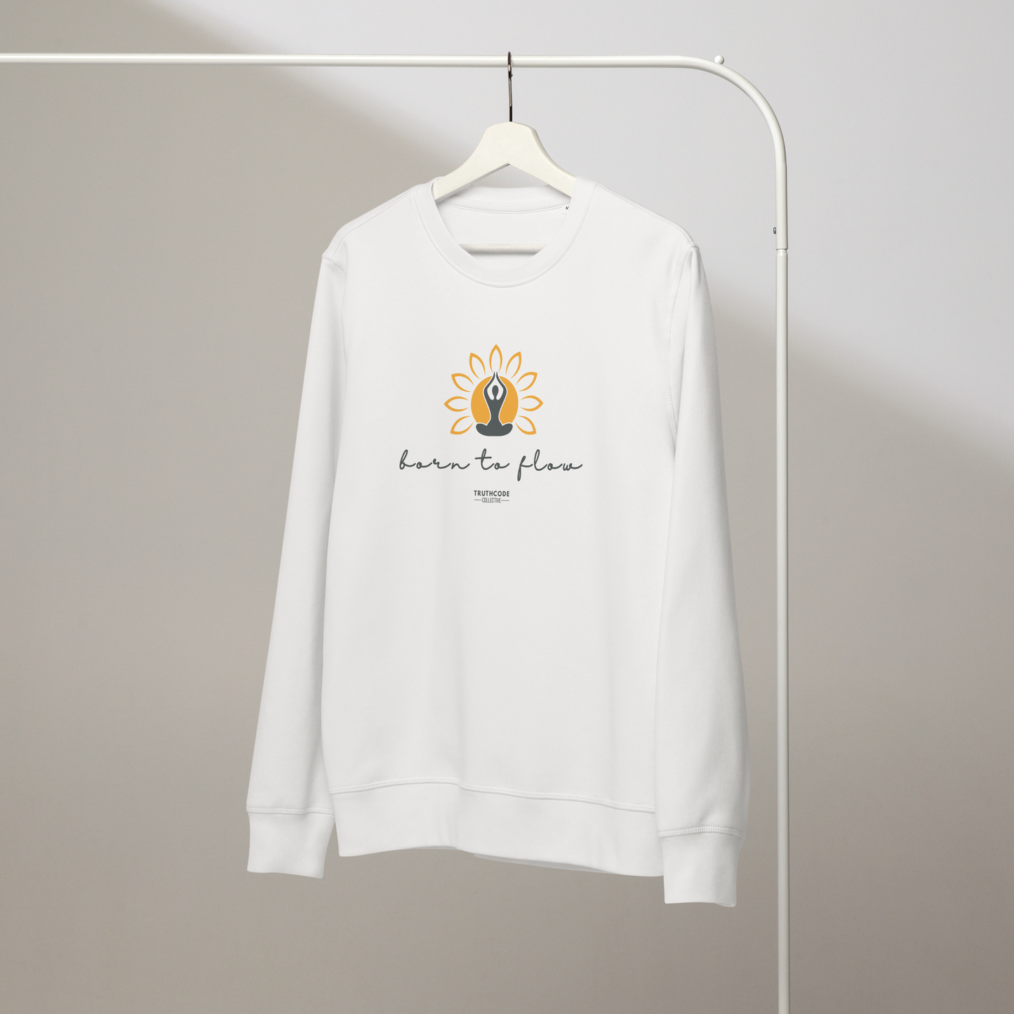 White organic sweatshirt with a flower design with person meditating design and 'born to flow' text on a hanger with a gray wall background