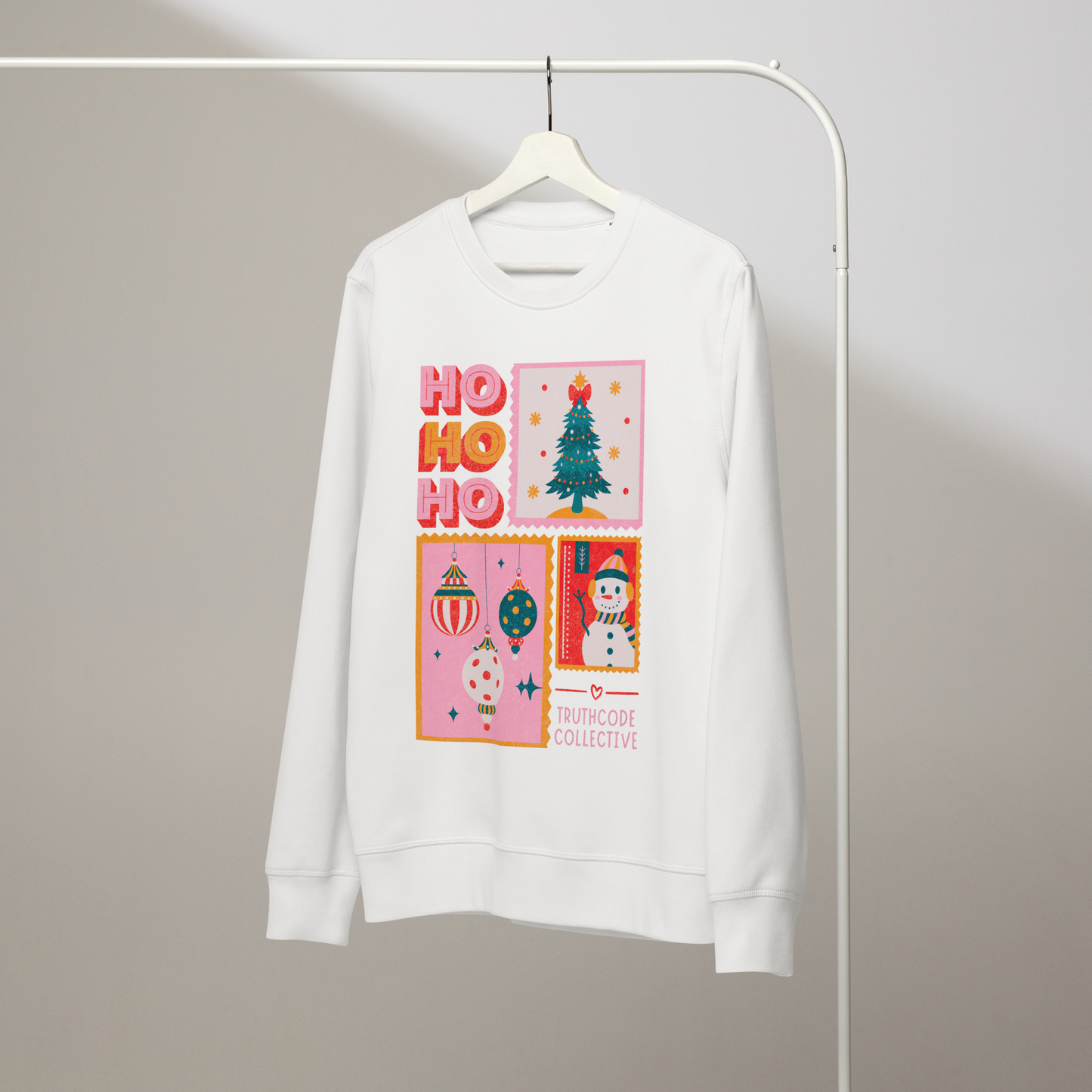 White organic sweatshirt with Christmas-themed design featuring 'HO HO HO' and Christmas postcard style graphic design on a hanger with a gray wall background