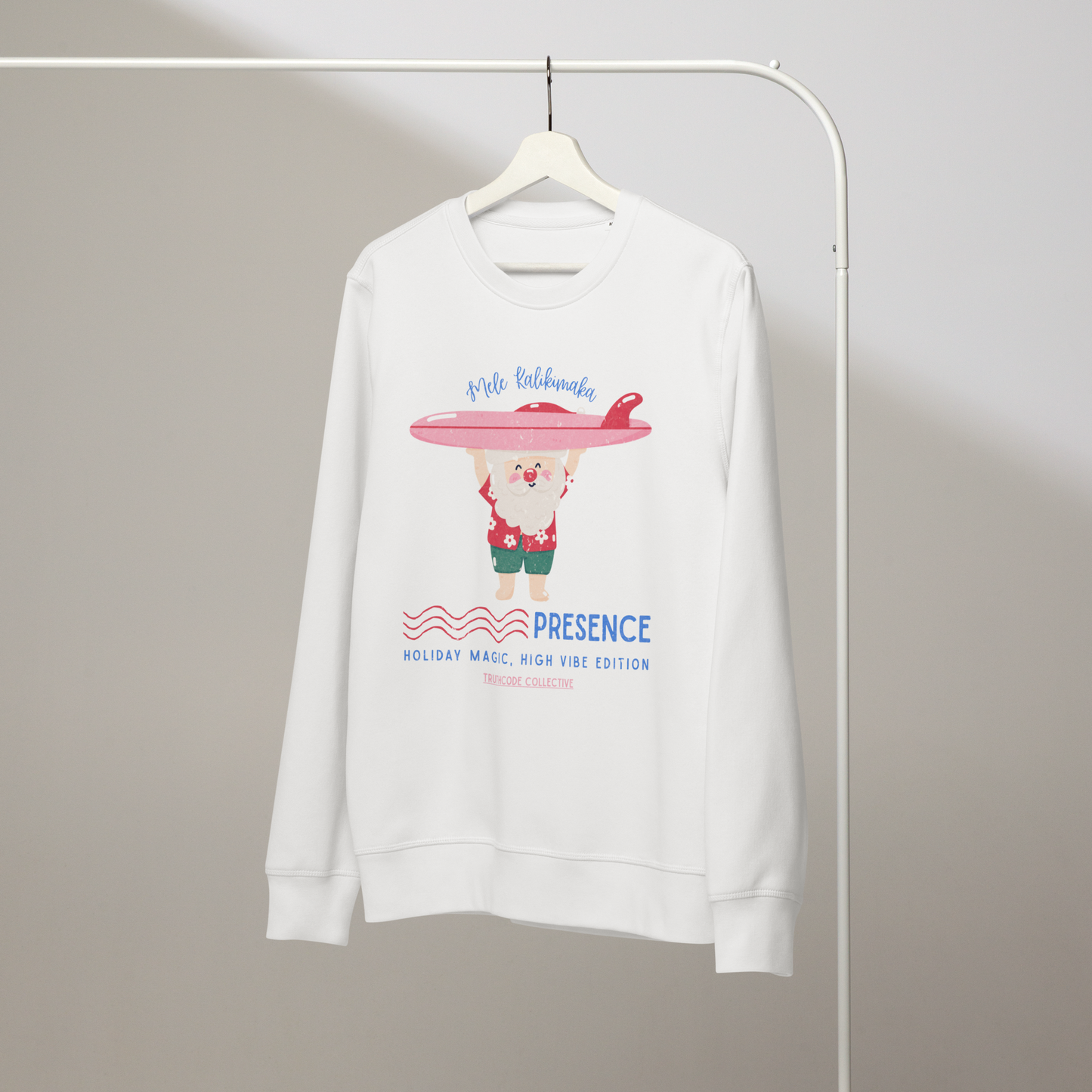 White organic sweatshirt with a Santa cartoon holding a surfboard and text 'Mele Kalikimaka' and 'Presence, holiday magic, high vibe edition' on a hanger with a gray wall background
