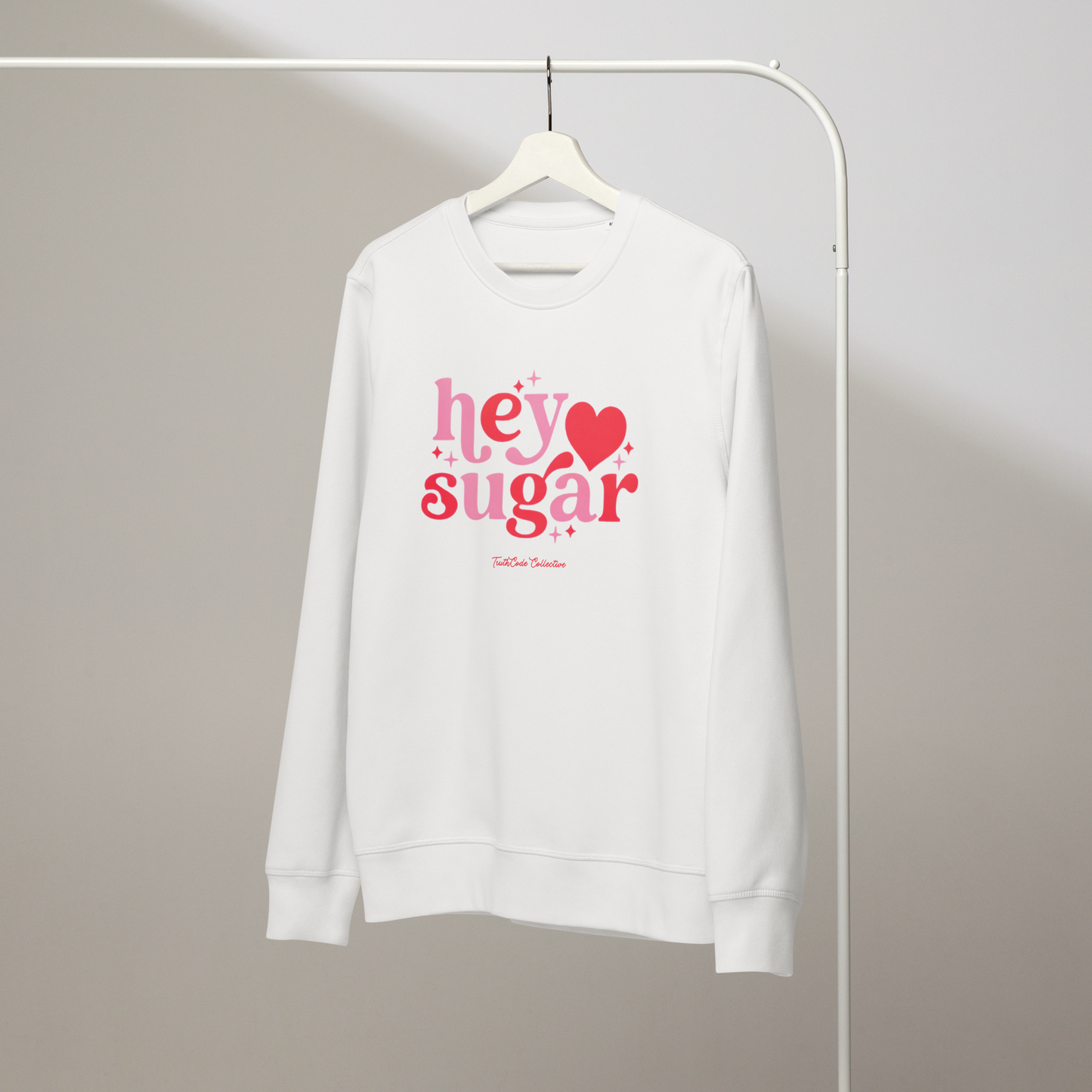 White organic sweatshirt with a floral heart design, on a hanger with a gray wall background