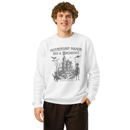 Model wearing beige organic sweatshirt with a graphic design of a haunted house, alien, and spaceship, with text 'Mothership Manor Bed & Breakfast' on a white background
