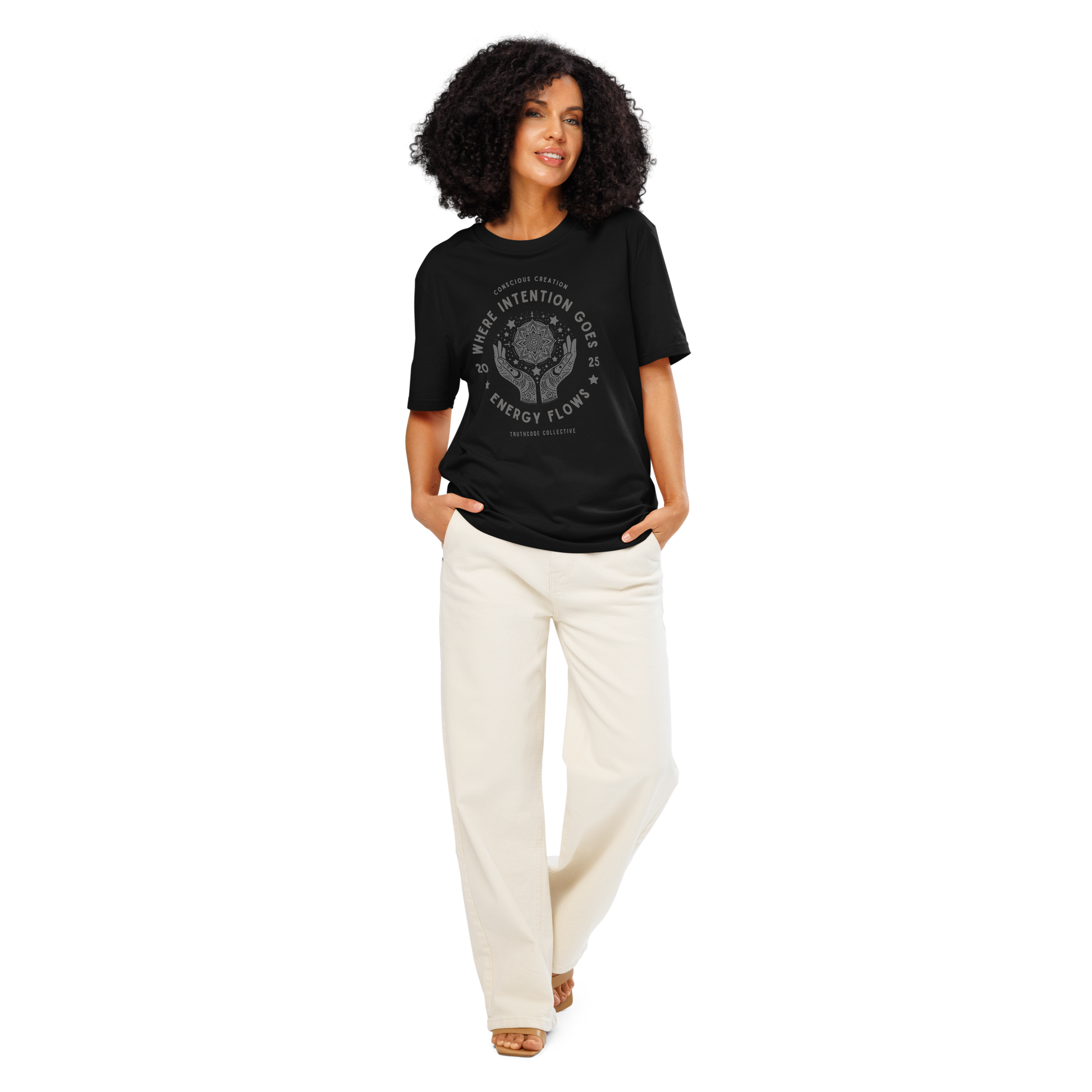 Woman wearing black organic t- shirt with a graphic of hands and stars around a mandala symbol, with text reading 'Where intention goes, energy flows'