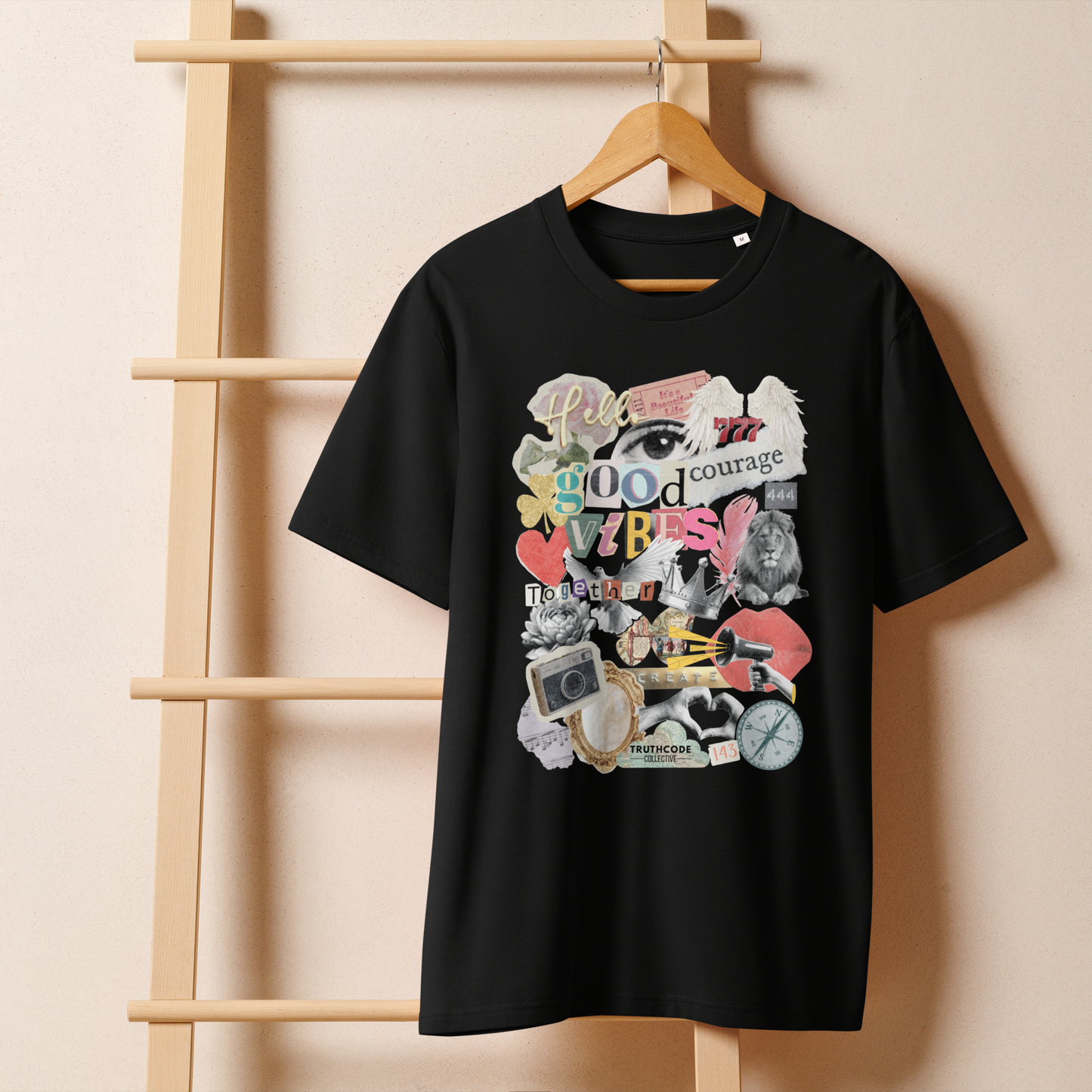 Black organic t-shirt with colorful collage graphic designs like a mood board on a wooden hanger with a beige wall in the background
