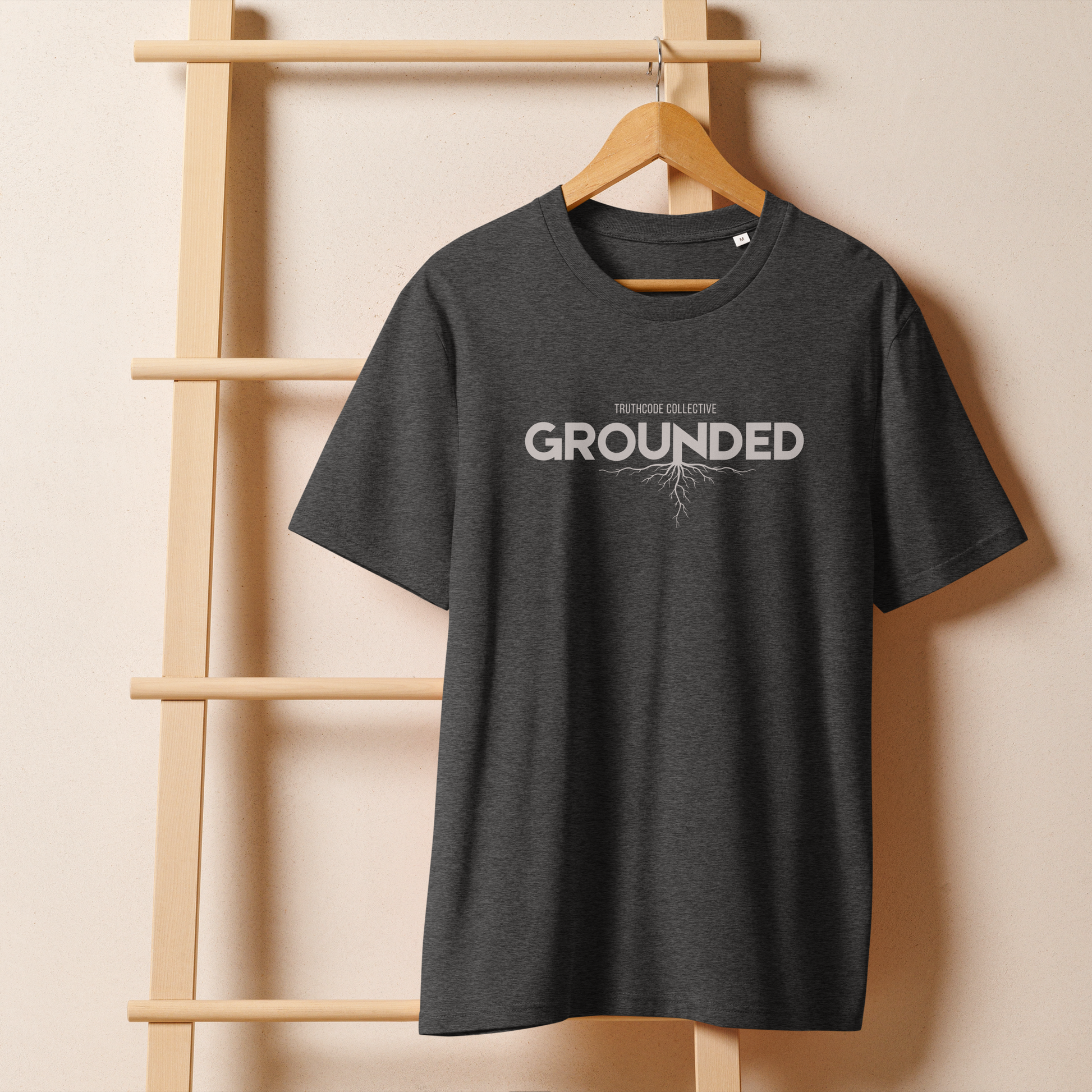 Gray organic t-shirt with 'GROUNDED' text and tree root graphic extending down hanging on a wooden hanger