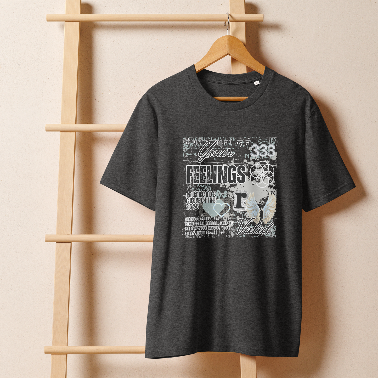 Dark gray organic t-shirt with white graphic collage type design and text 'Your feelings  r valid' on a wooden hanger with a beige wall background