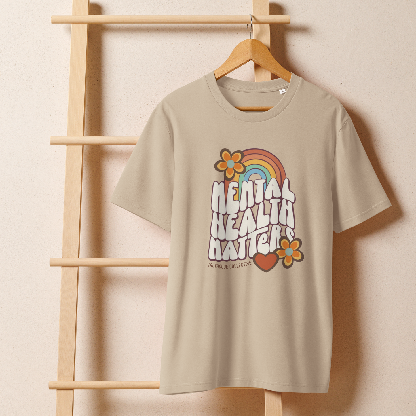 Beige organic t-shirt with 'Mental Health Matters' graphic design featuring a rainbow and flowers hanging from a wooden hanger