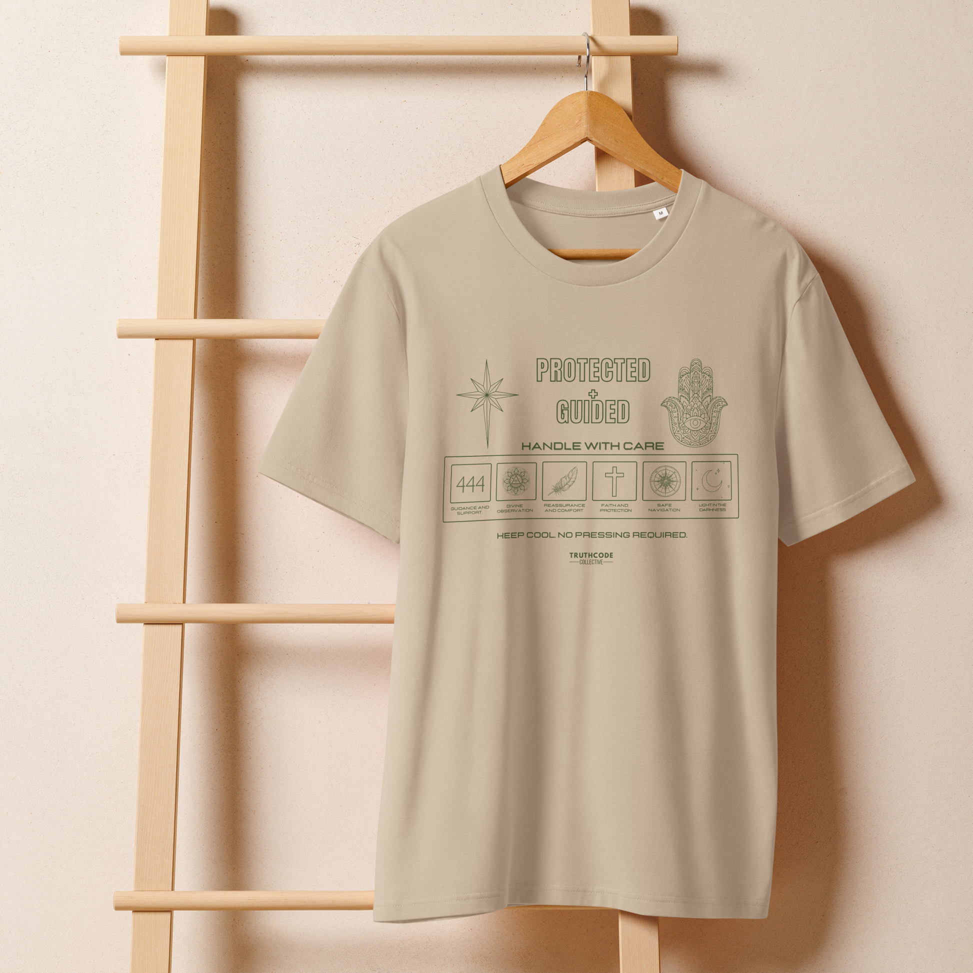 Beige organic t-shirt with text 'Protected + guided'  with symbols and graphics relating to it on a wooden hanger with a beige wall background