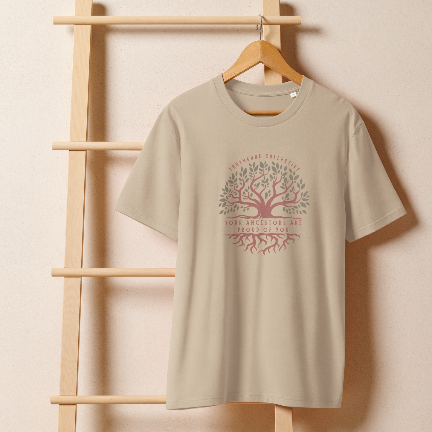 Beige organic t-shirt with a tree design and text 'Your ancestors are proud of you' on a wooden hanger with a beige wall background