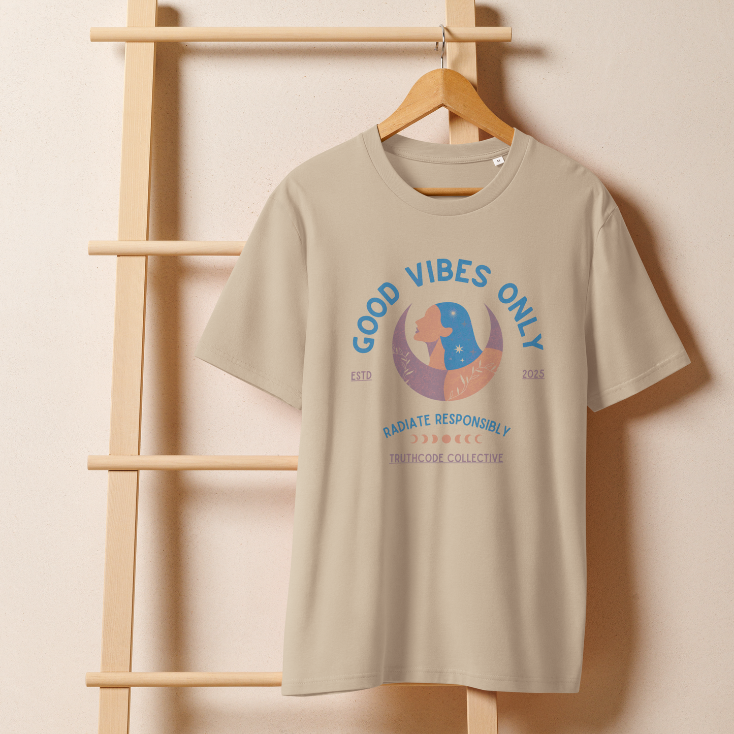 Beige organic t-shirt with text 'Good Vibes Only' and 'Radiate responsibly' woman and moon graphic design on a wooden hanger with beige wall background