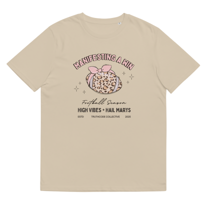 Beige organic t-shirt with girly football graphic design and text 'Manifesting a win, high vibes and hail marys' on a white background