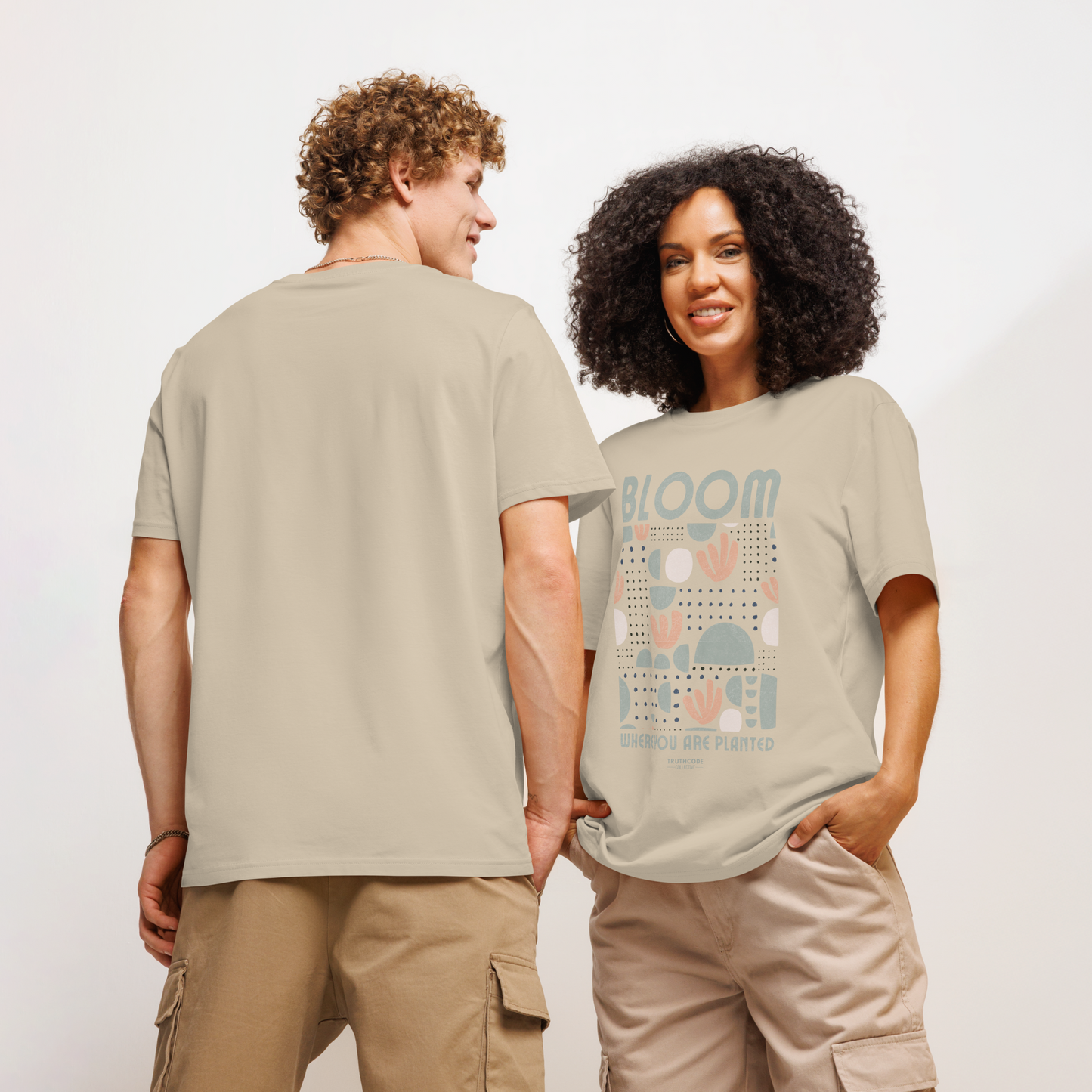Models wearing beige organic t-shirt with 'Bloom Where You Are Planted' design on a white background