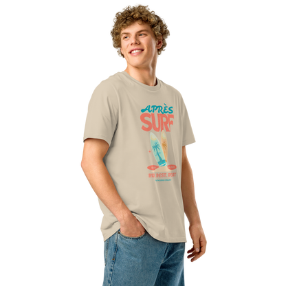 Person wearing a beige organic t-shirt with a surfing graphic design and text 'Après surf' on a white background