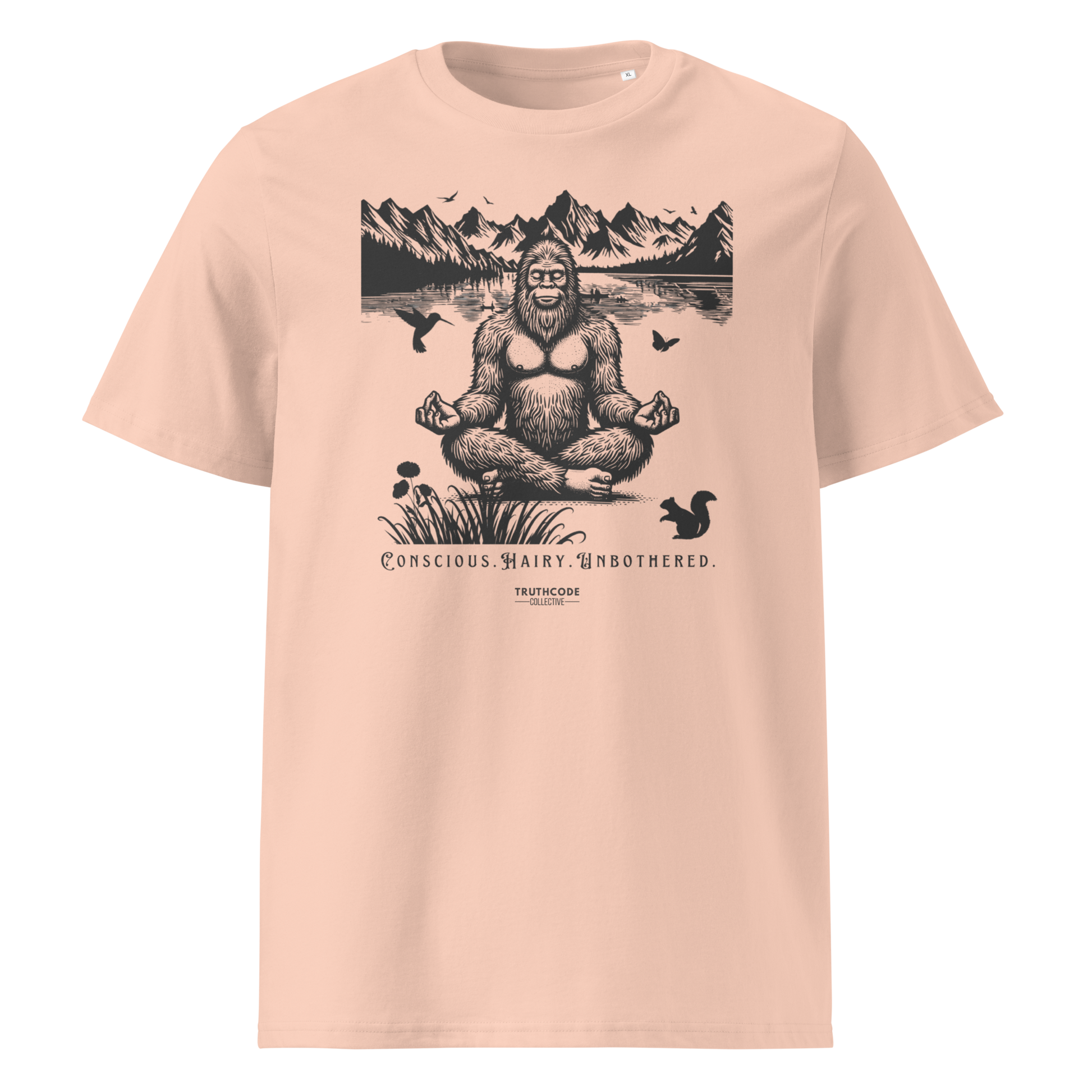 Pink organic t-shirt with a graphic of a meditating Sasquatch in a mountain setting and text reading 'Conscious, hairy, and unbothered' 