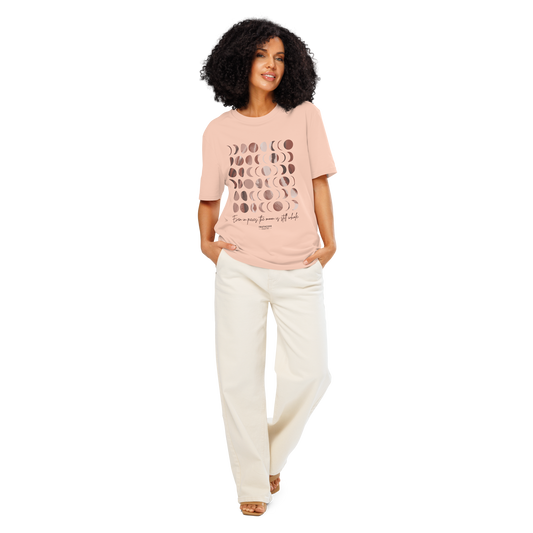 Woman wearing peach organic t-shirt with rose gold moon phase design and text 'Even in pieces, the moon is still whole' on a white background