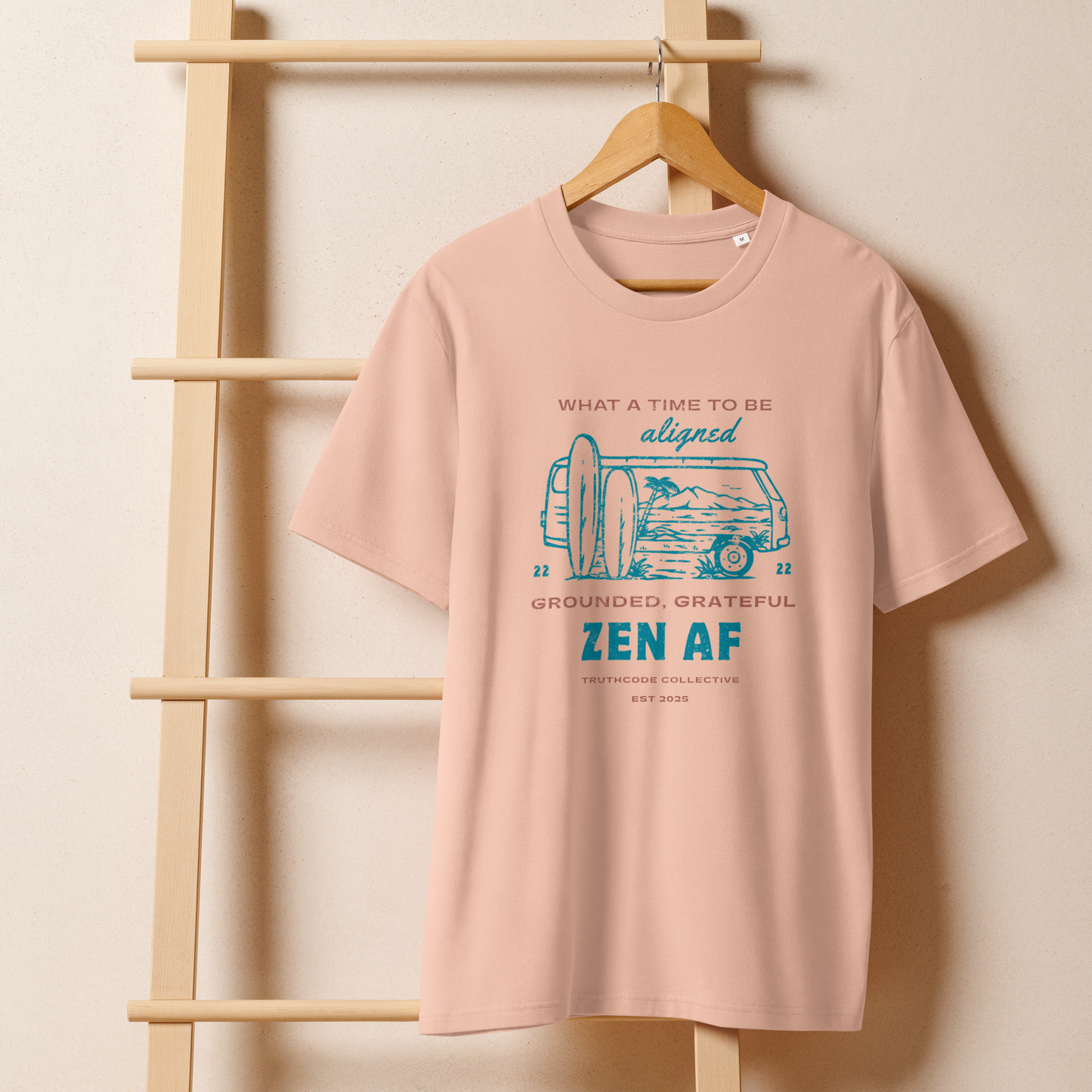 Peach organic t-shirt with a graphic design  of vintage surf van and text 'What a time to be aligned, grounded, grateful, zen AF' on a wooden hanger with a beige wall background