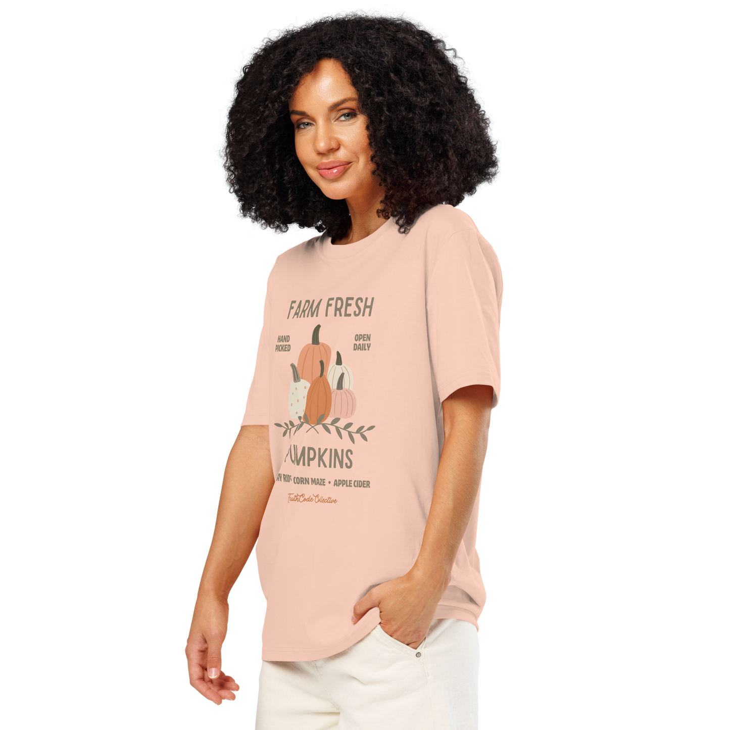 Woman wearing peach organic t-shirt with pumpkin graphic and text 'Farm fresh pumpkins, hay rides, corn maze, apple cider'  on a white background