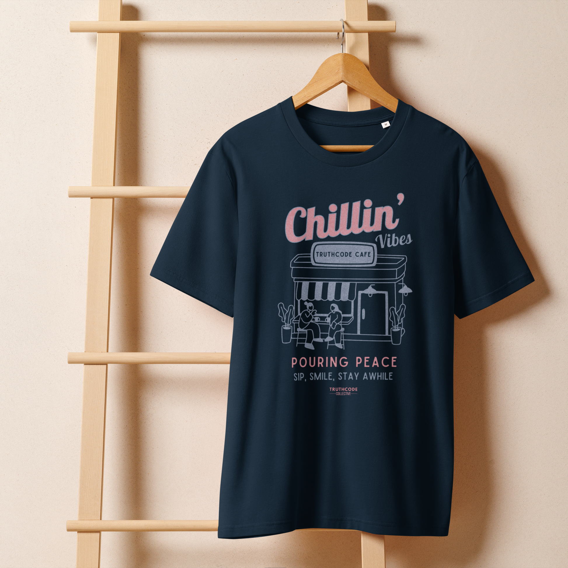 Navy blue organic t-shirt with 'Chillin' Vibes, TruthCode Cafe' and 'Pouring peace, sip, smile, stay a while' graphic design on a wooden hanger with a beige wall background