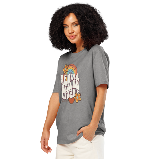 Woman wearing gray organic t-shirt with 'Mental Health Matters' graphic design featuring a rainbow, flowers, and heart on a white background.