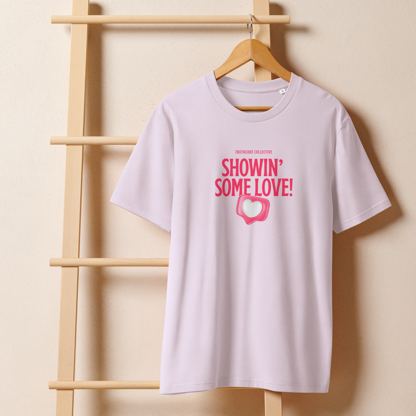 Lavender organic t-shirt with pink text 'Showin' some love!' and heart graphic on a hanger with a beige wall background