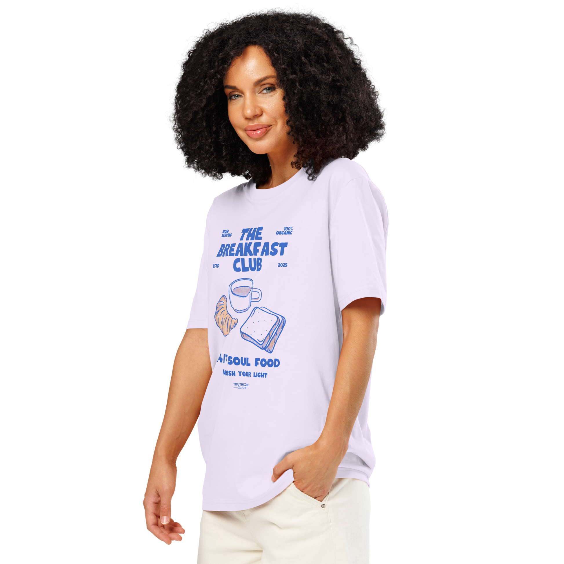 Woman wearing lavender organic t-shirt with 'The Breakfast Club' graphic design featuring a coffee cup, croissant, and sandwich.