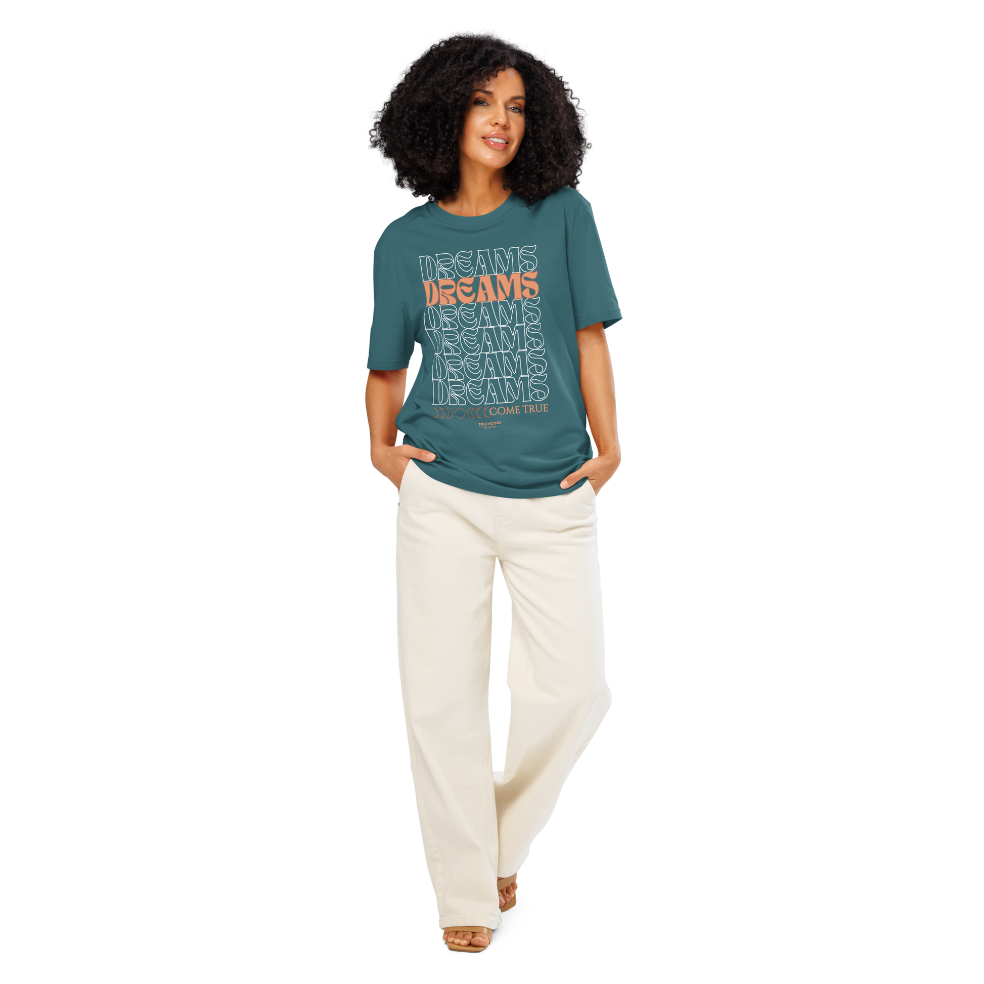 Woman wearing a teal organic t-shirt with text 'Dreams come true' and white pants on a white background