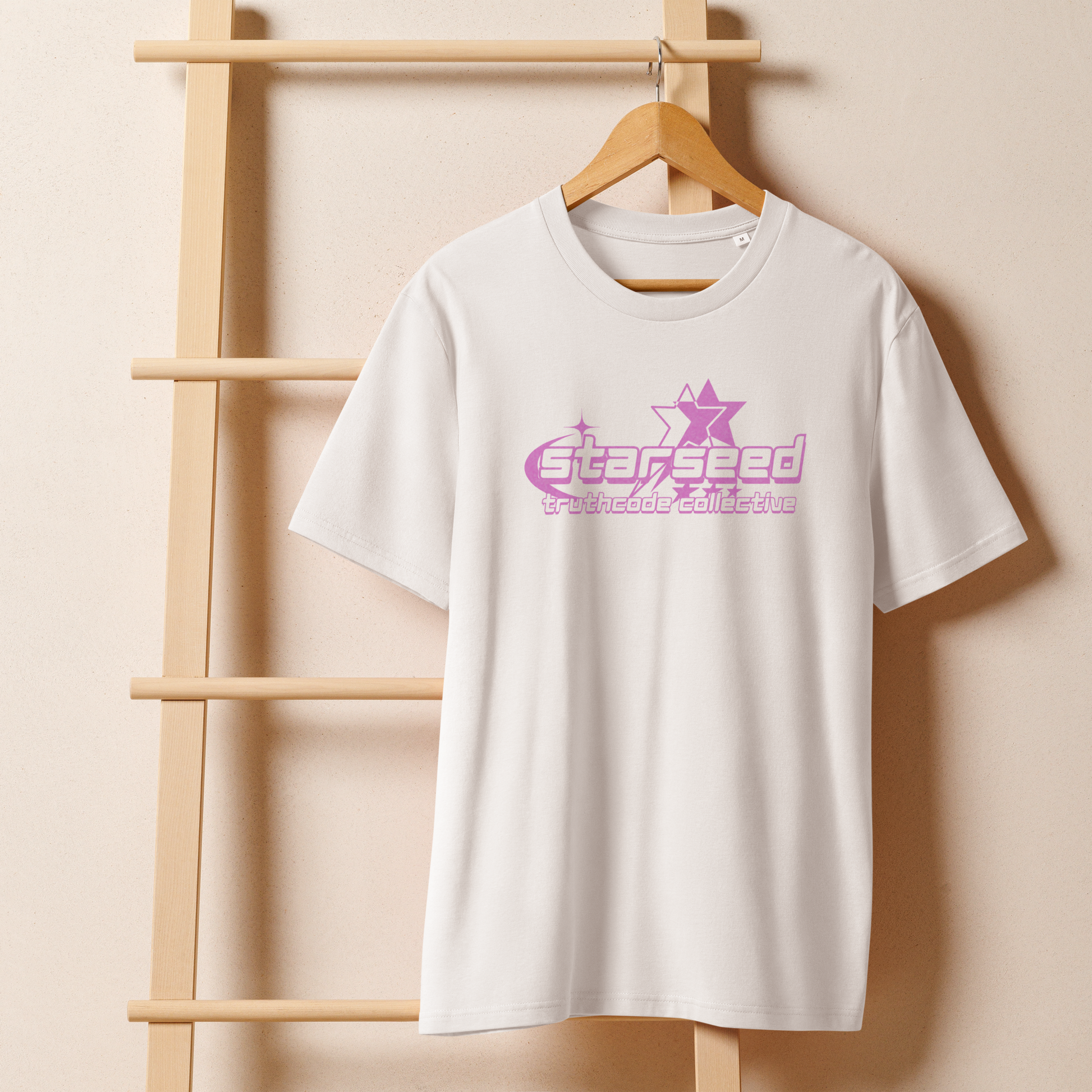 White organic t-shirt with a purple star graphic and  text 'Starseed' on a wooden hanger with beige wall in the background