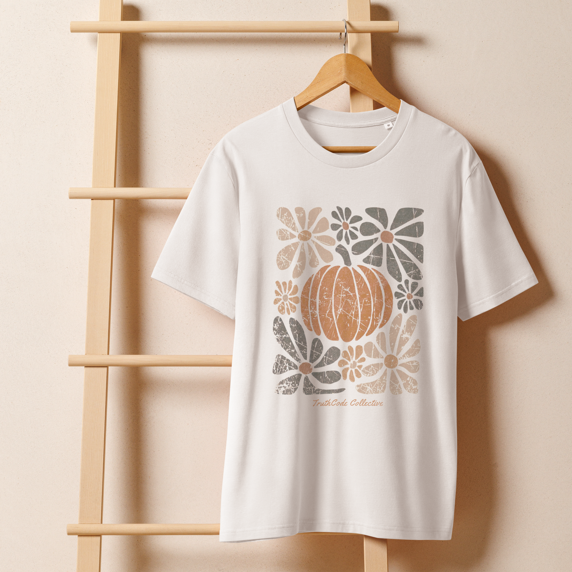 White organic t-shirt with pumpkin and floral design on a wooden hanger against a beige wall.