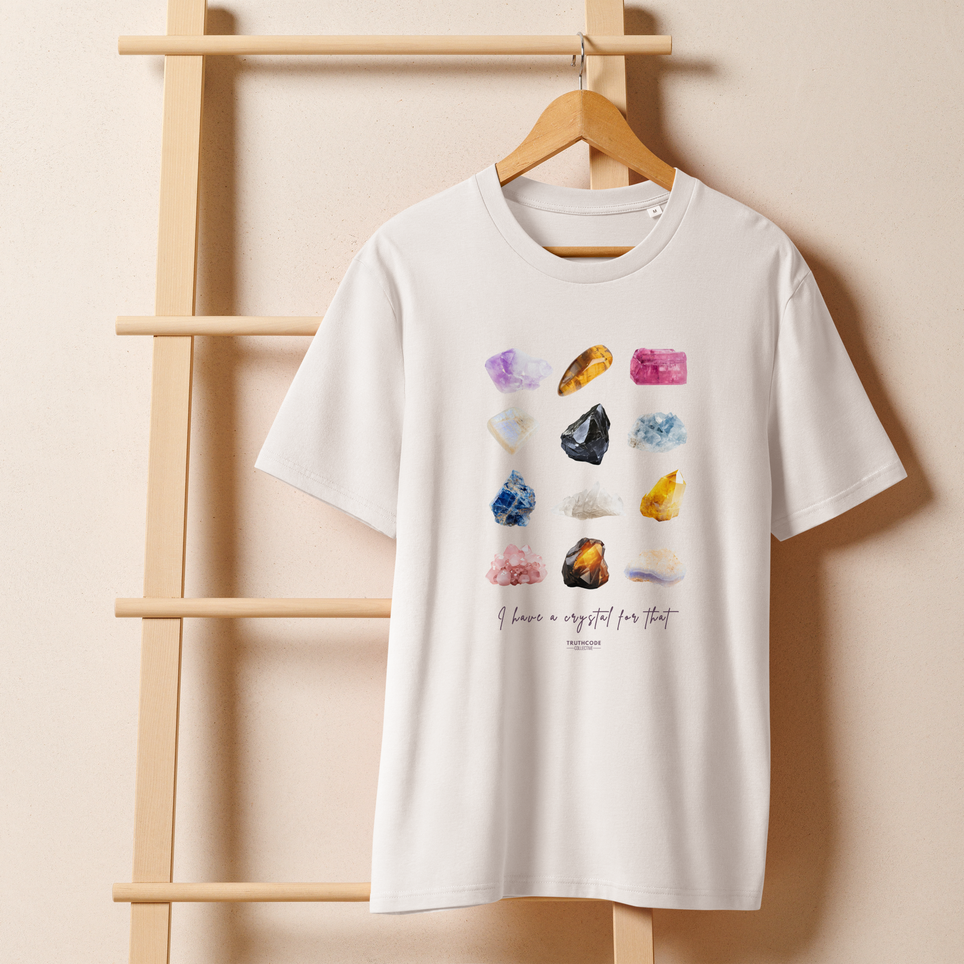 White organic t-shirt with colorful crystal graphics and text 'I have crystals for that' on a wooden hanger with a gray wall background