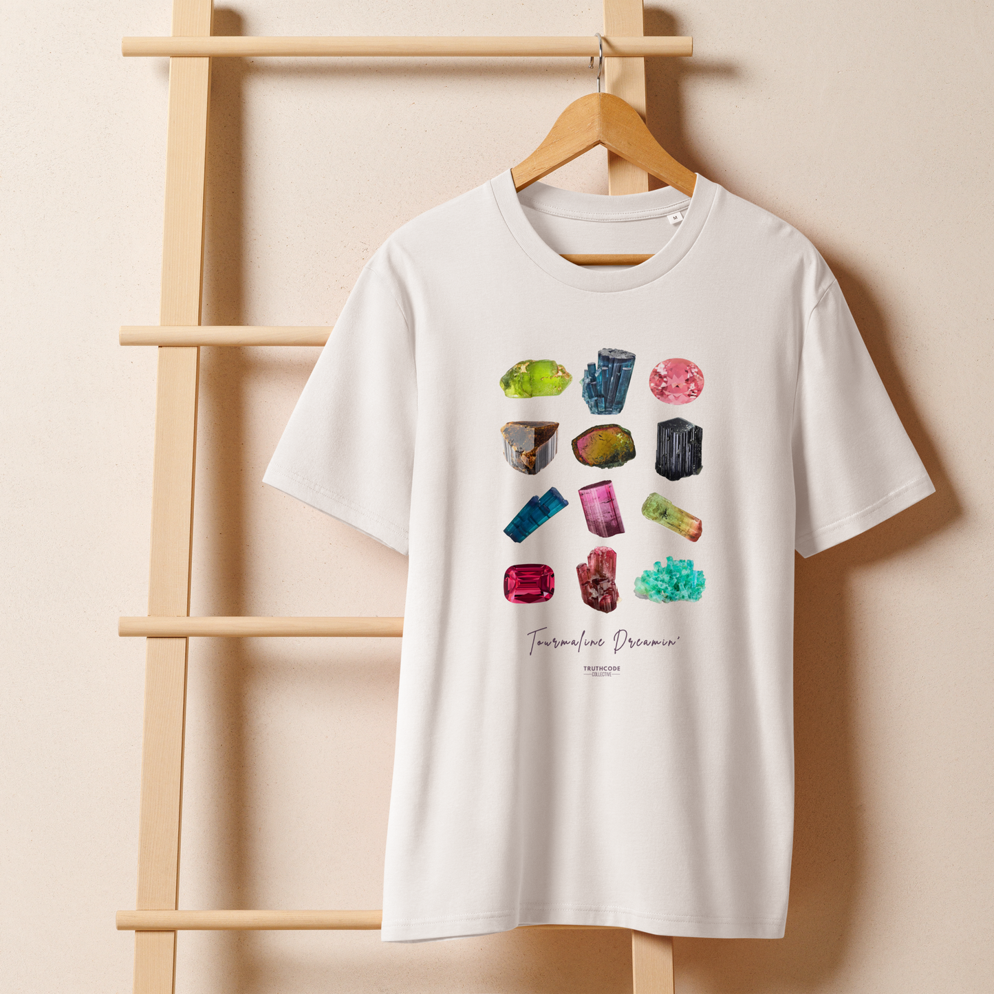 White organic t-shirt with gemstone graphic and text 'Tourmaline Dreamin'  on a wooden hanger against a beige wall.
